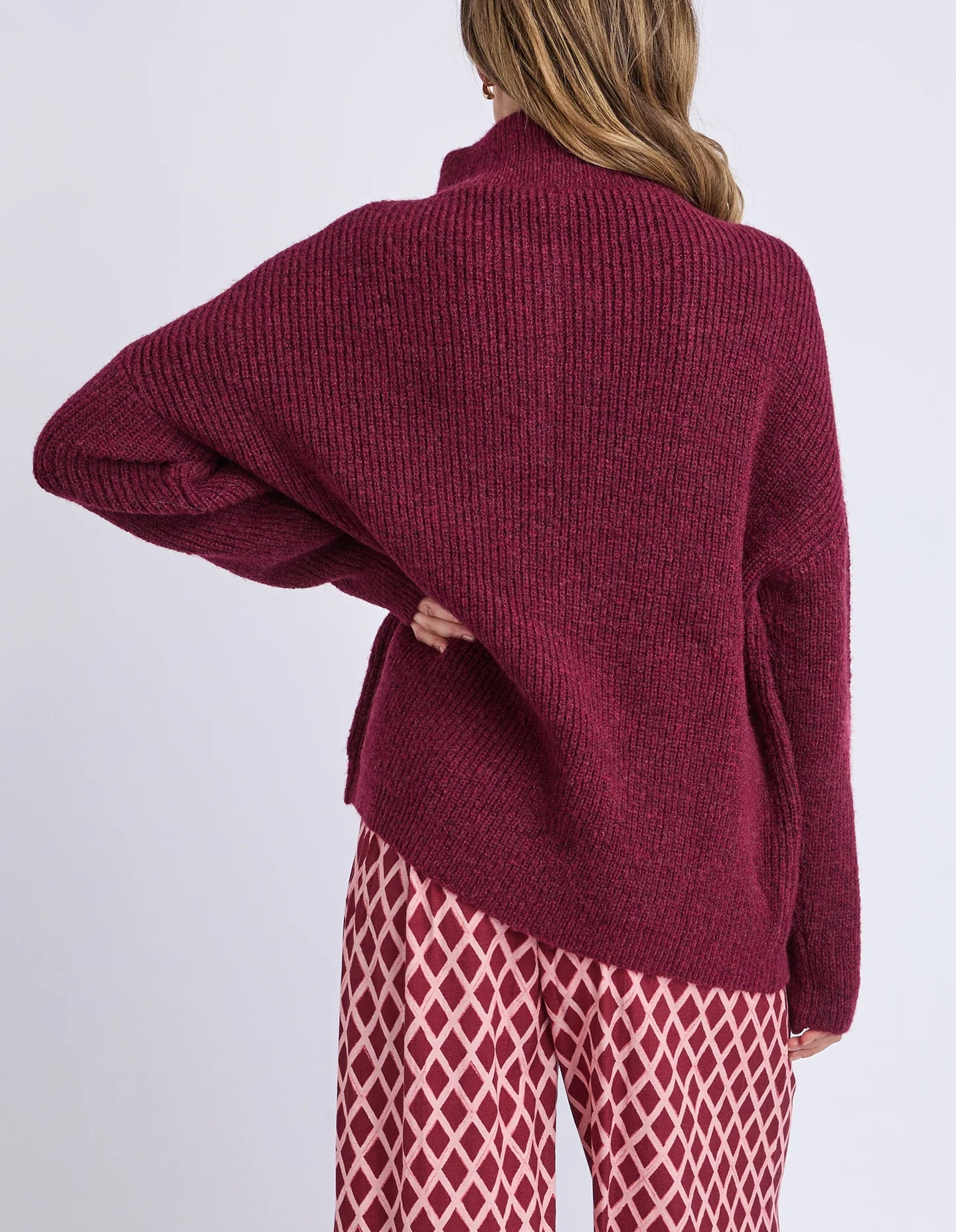 Woman wearing a burgundy sweater and patterned pants on a white background
