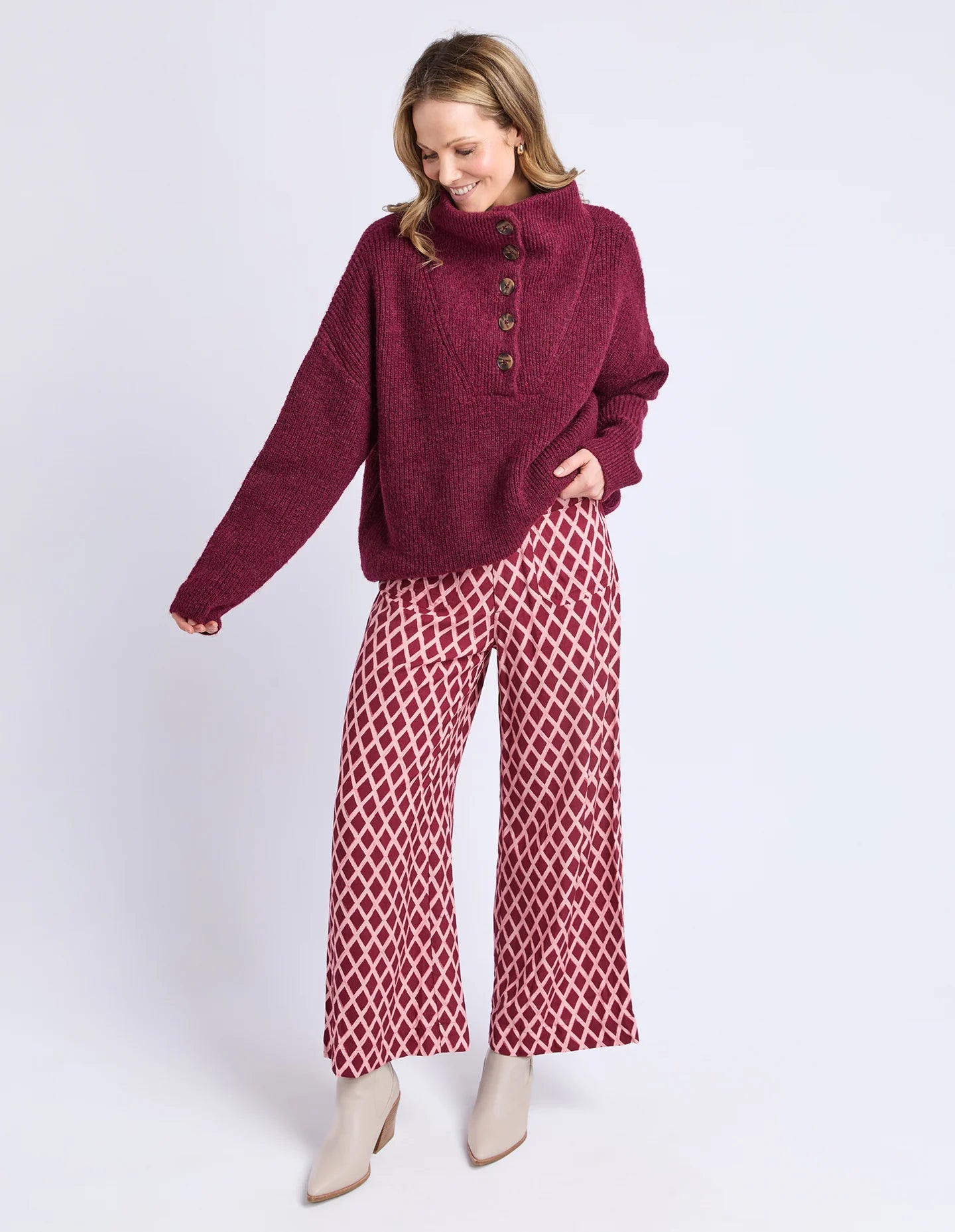 Woman wearing a Elm burgundy sweater and patterned skirt on a light gray background