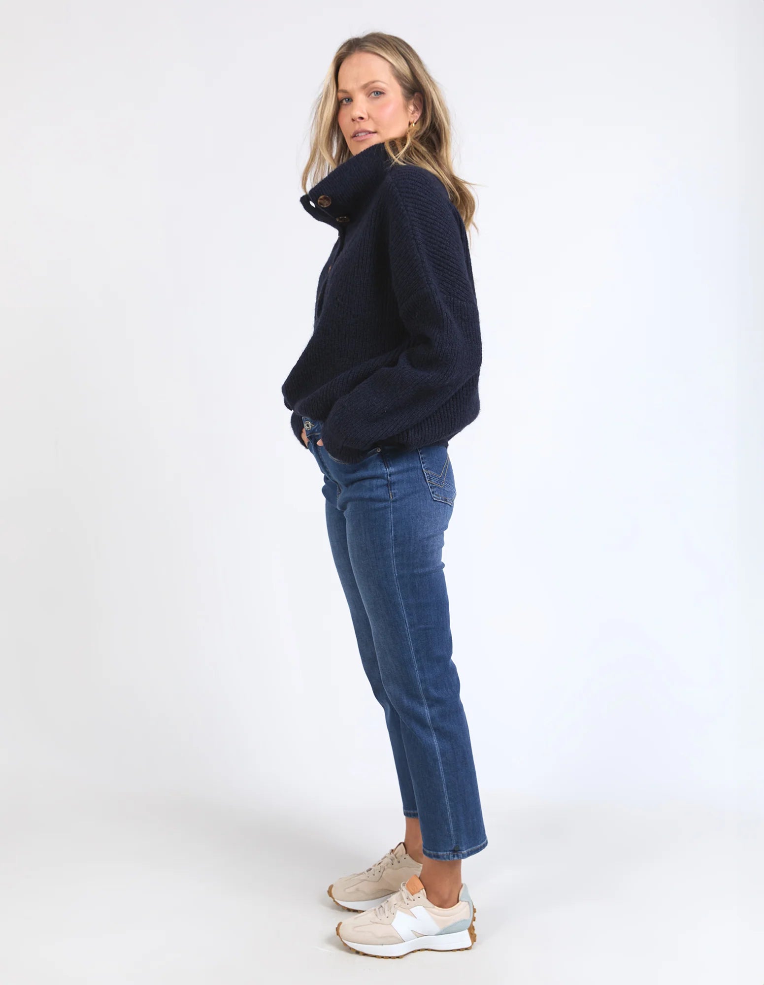 Woman wearing a Elm navy sweater and blue jeans on a white background