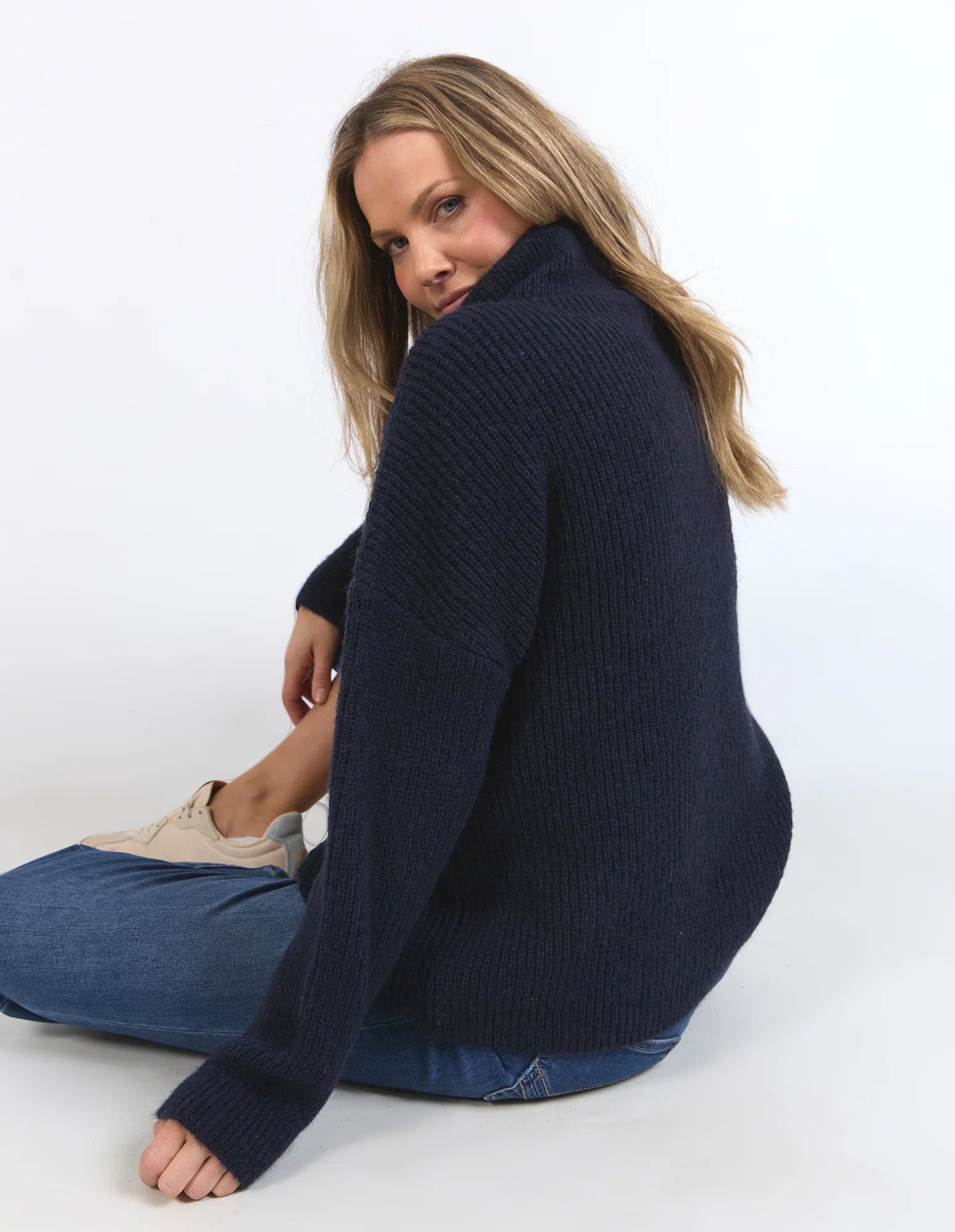 Woman wearing a Elm navy blue sweater sitting on a white background