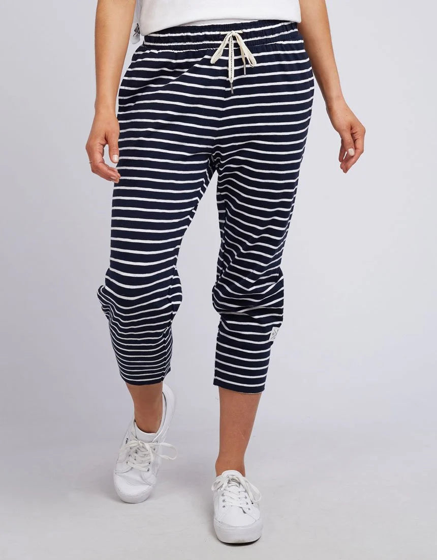 A woman wearing Elm navy and white horizontally striped cropped pants with a cream drawstring, paired with white sneakers, shown against a light gray studio background.