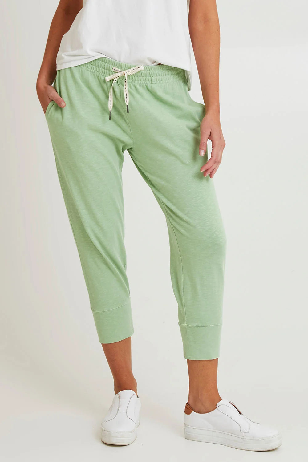 Image of A woman wearing Elm light mint green cropped jogger pants with an elastic drawstring waist, paired with a white top and white slip-on sneakers, against a plain light background.