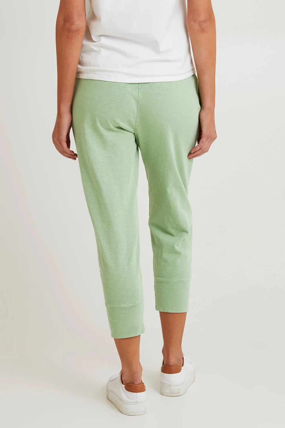 Image of A woman shown from the back wearing Elm light mint green cropped jogger pants, a white top, and white sneakers against a plain light background.