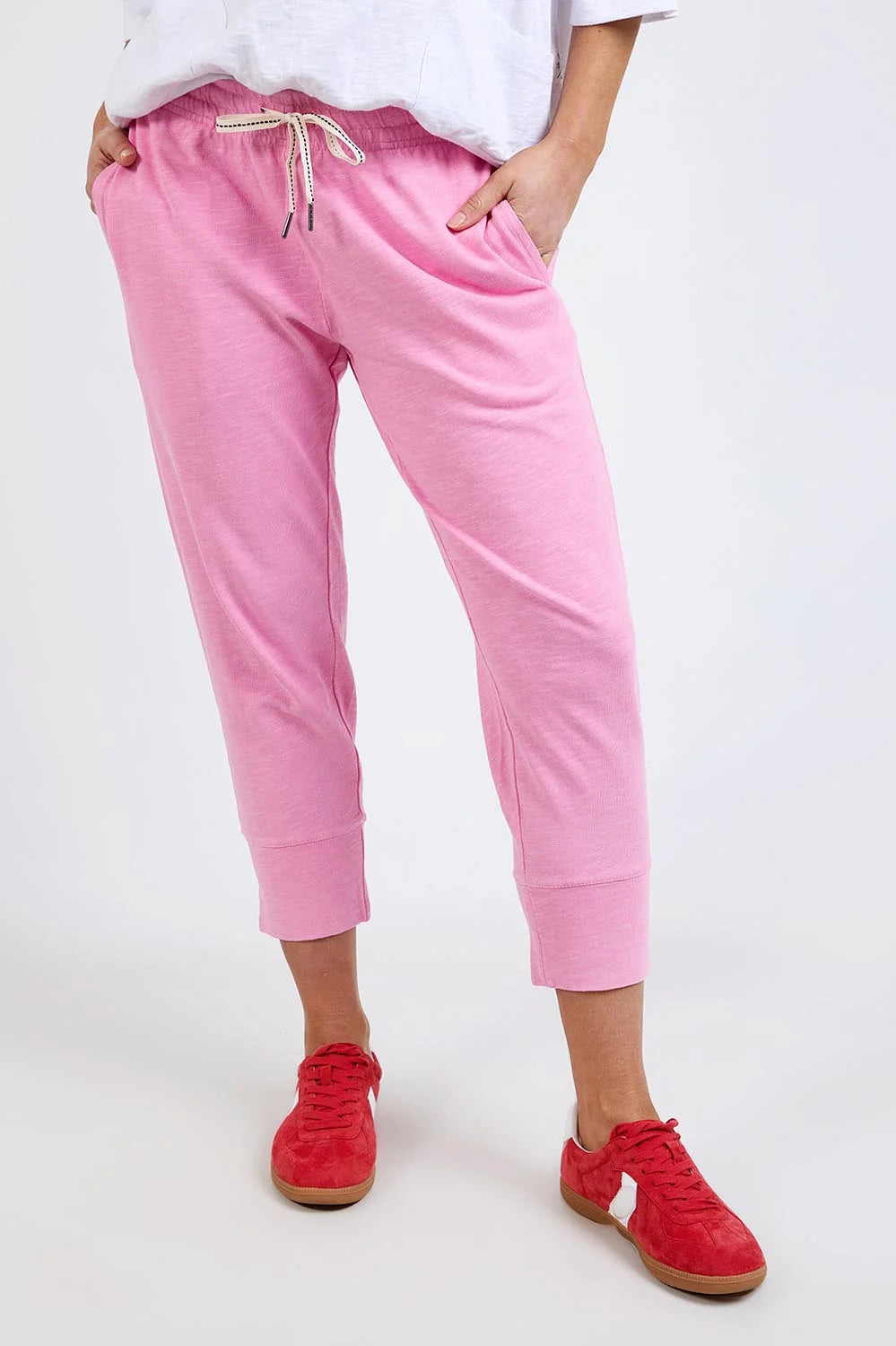 Elm pink cropped sweatpants with a drawstring waist and side pockets, shown on a model wearing red sneakers against a plain white studio background.
