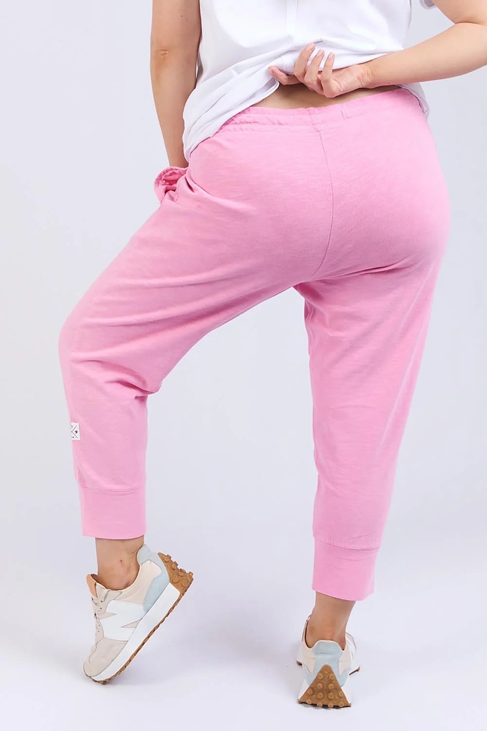 Image of Elm pink jogger pants modeled from the back, featuring a drawstring waist and elastic cuffs, paired with a white t-shirt and sneakers on a light gray background.