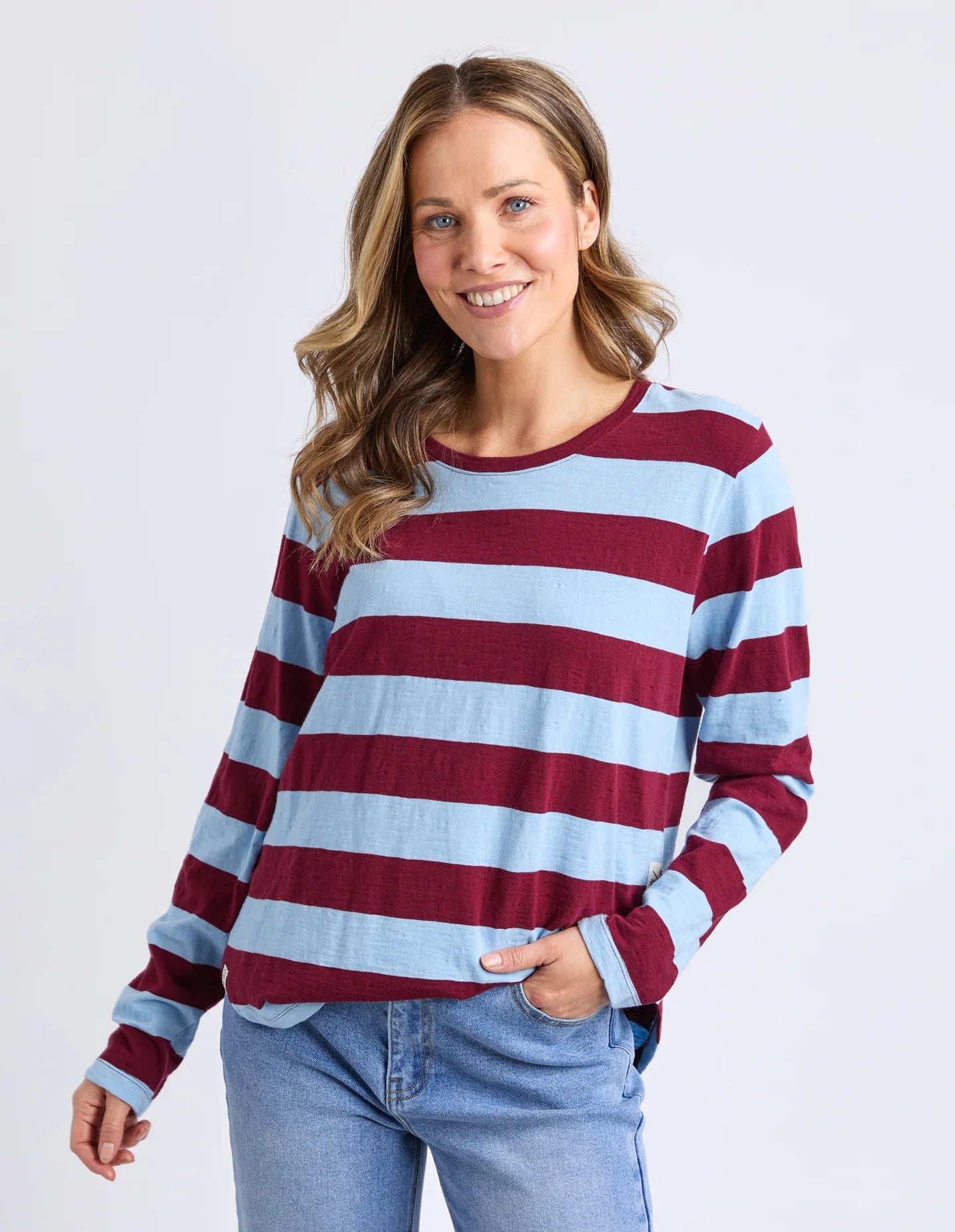 Image of Woman wearing a Elm maroon and light blue striped sweater with jeans on a white background
