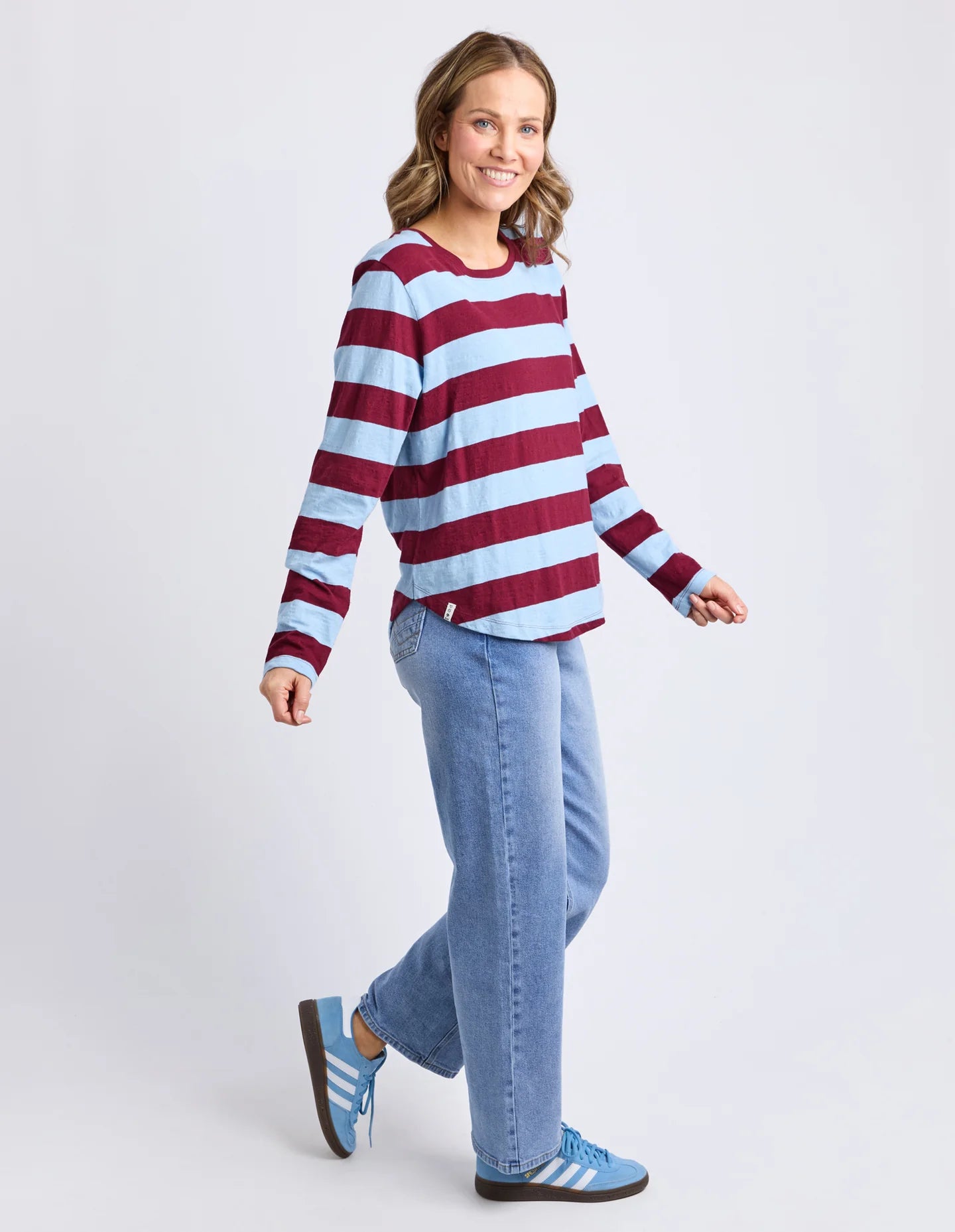 Image of Woman wearing a Elm red and white striped sweater and blue jeans on a light gray background