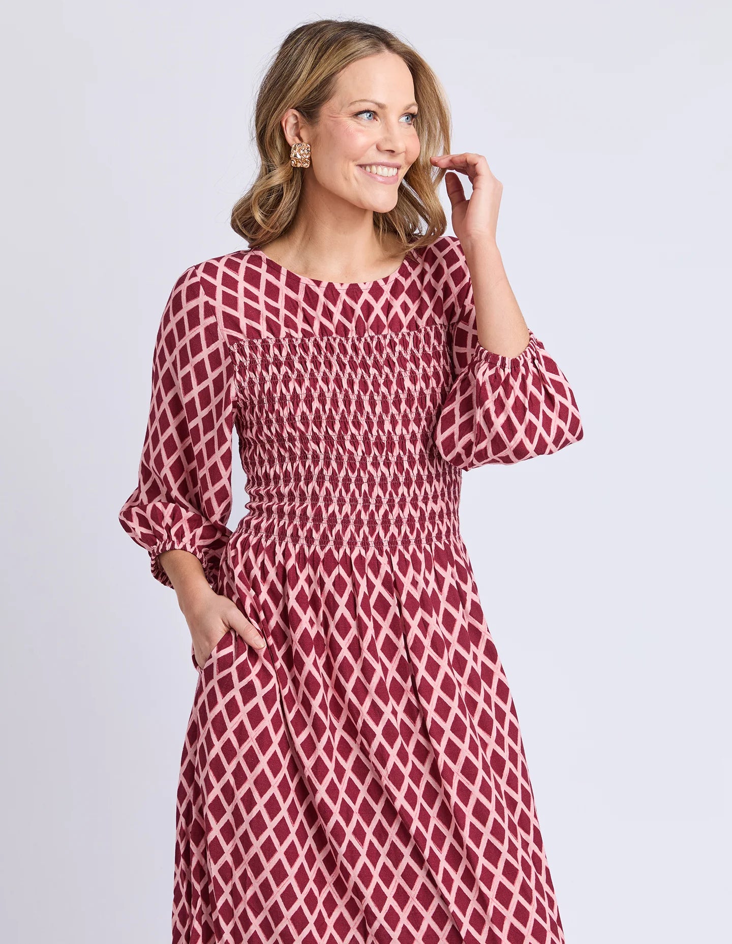 Image of Woman wearing a Elm red patterned dress against a light gray background
