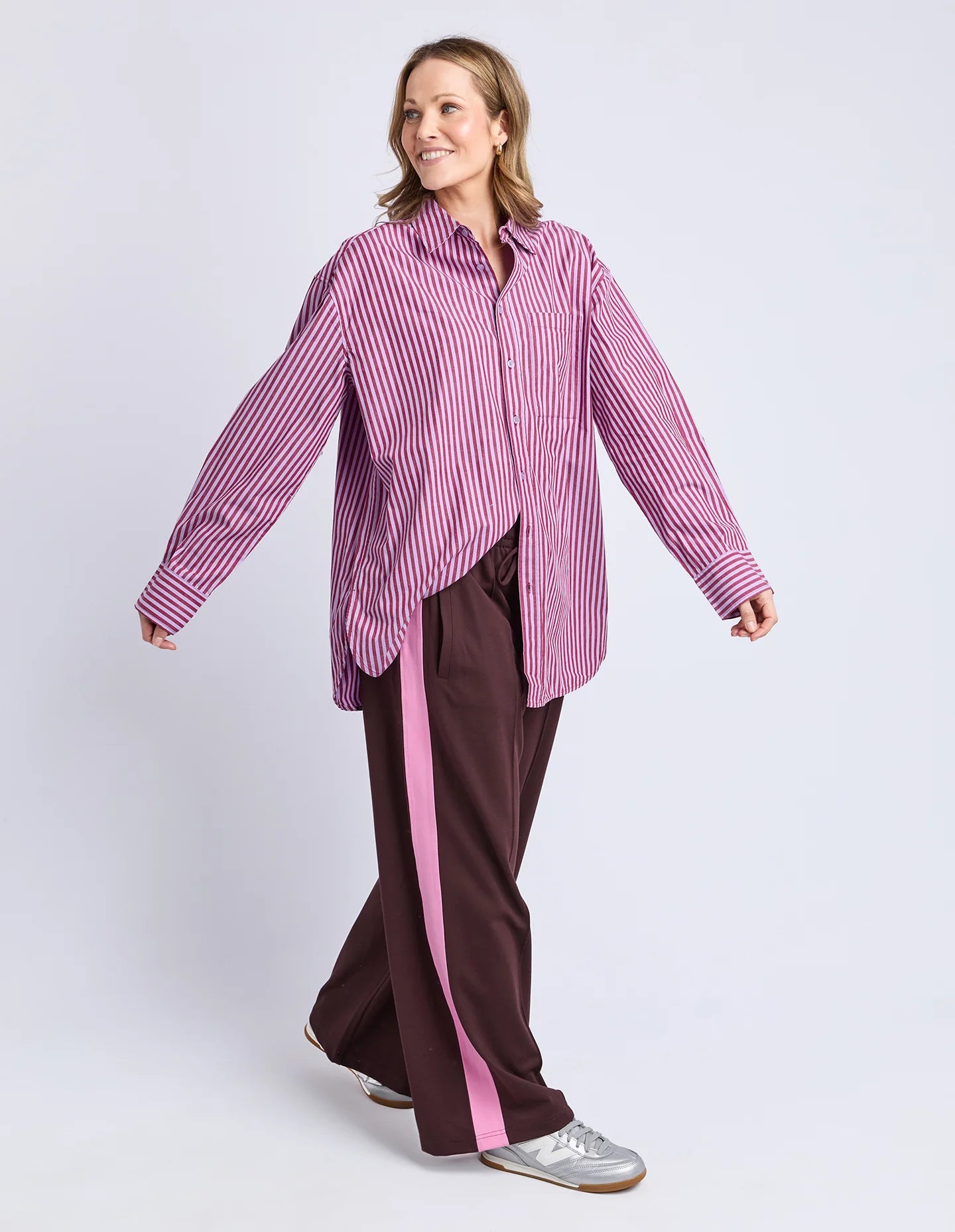 Image of Woman wearing a Elm pink and white striped shirt with brown pants on a light gray background
