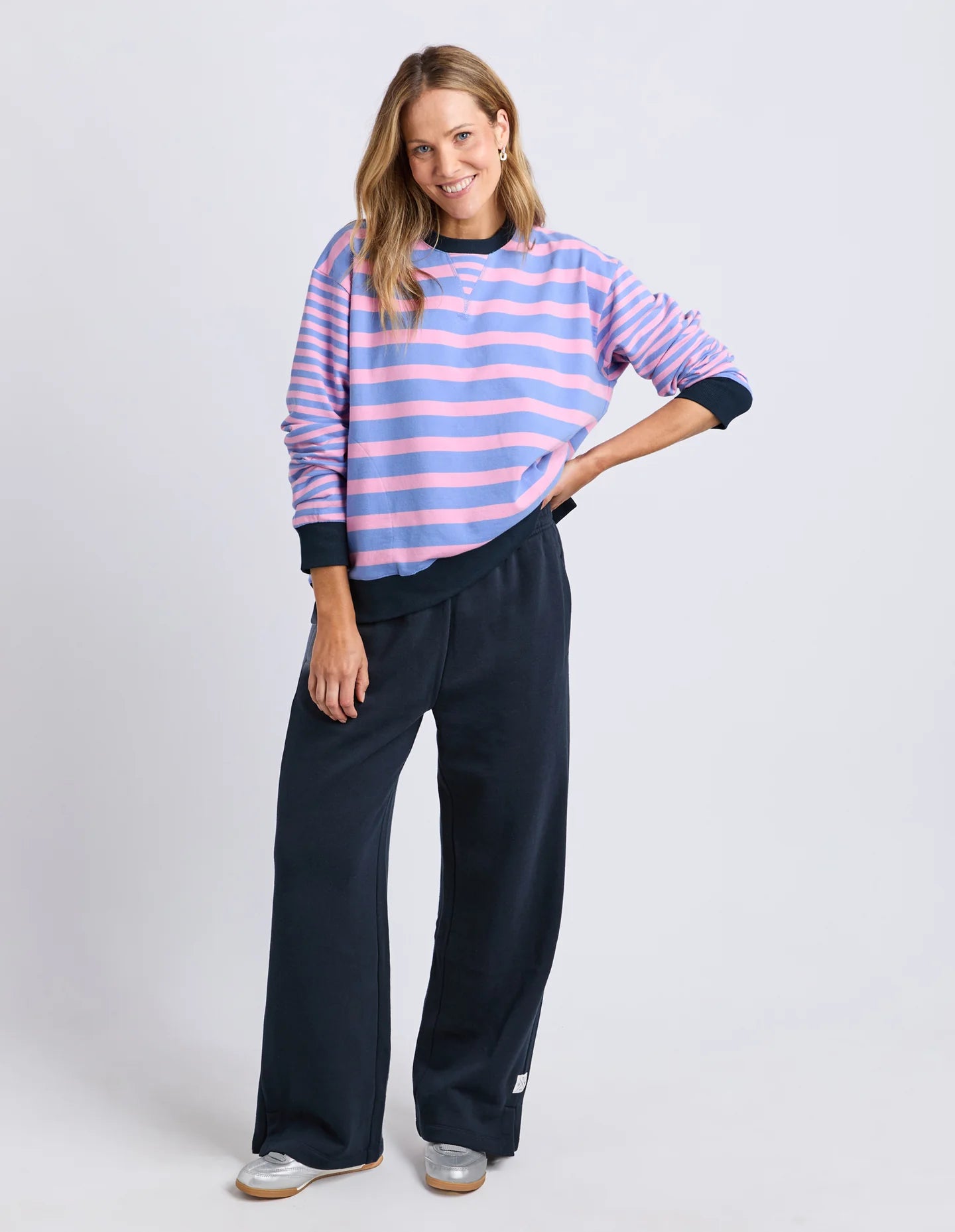Image of Woman wearing a striped sweater and Elm navy pants on a white background