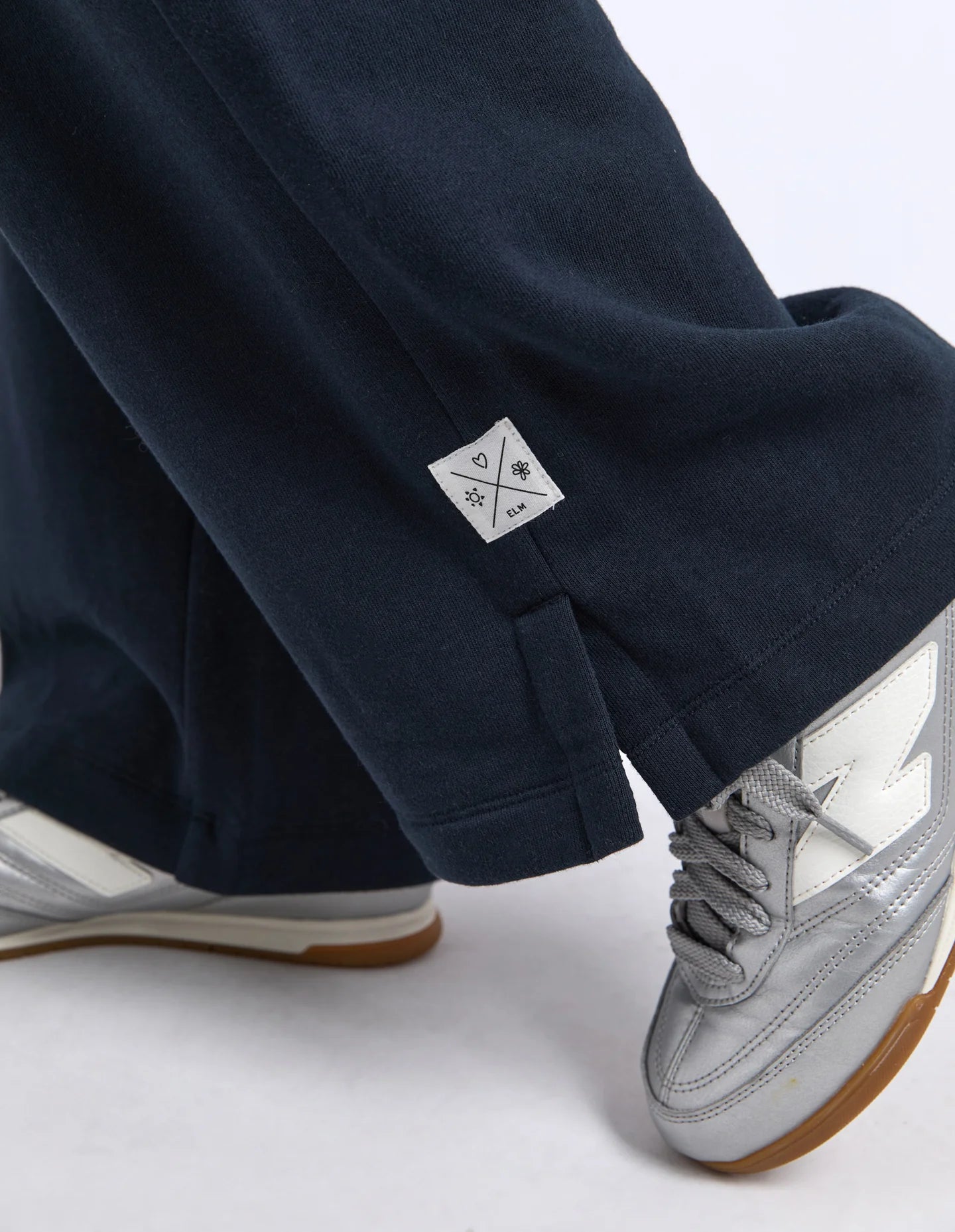 Image of Elm navy pants with a logo on the pocket and silver sneakers on a white background