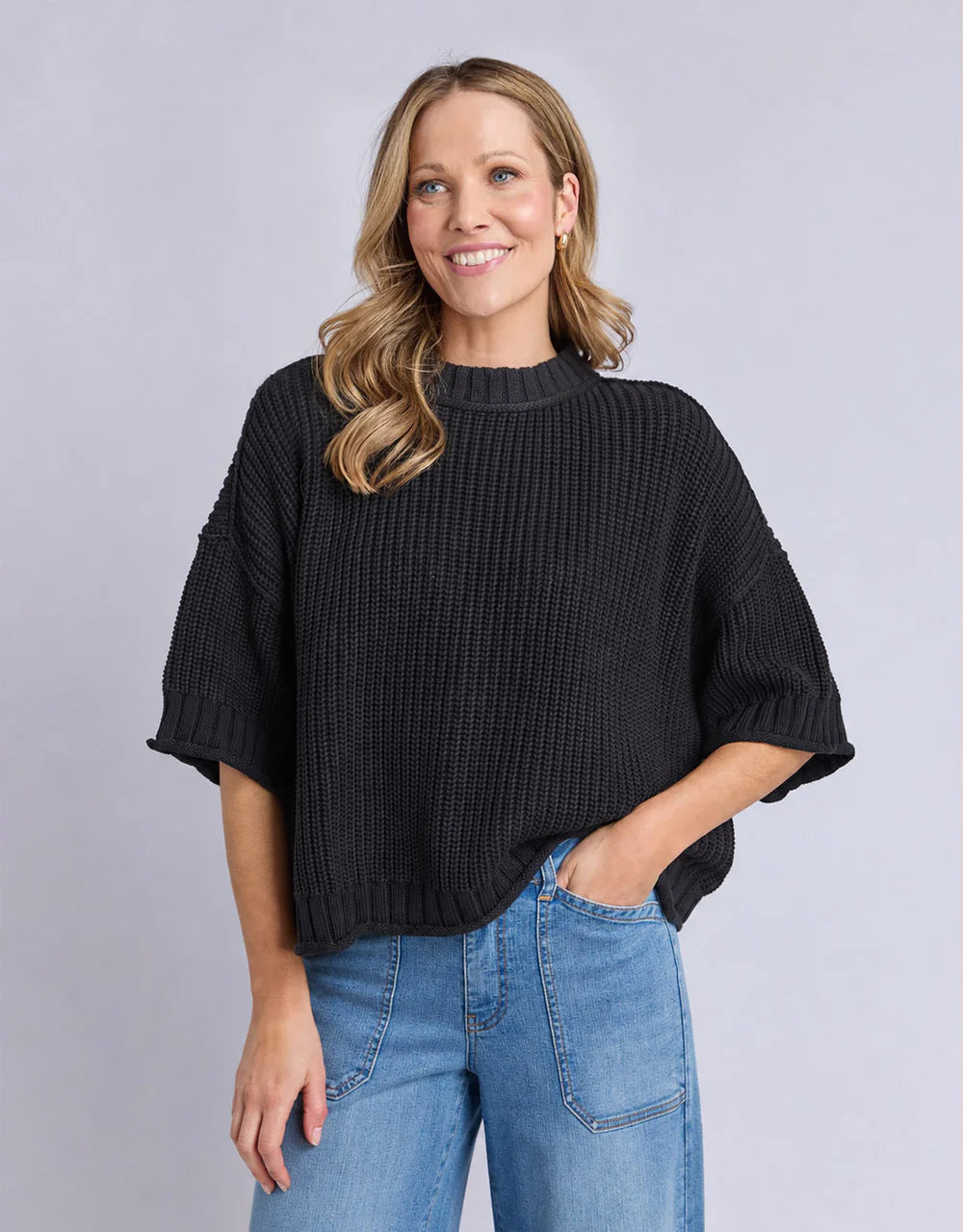 Image of Woman wearing a Elm black sweater and blue jeans against a gray background