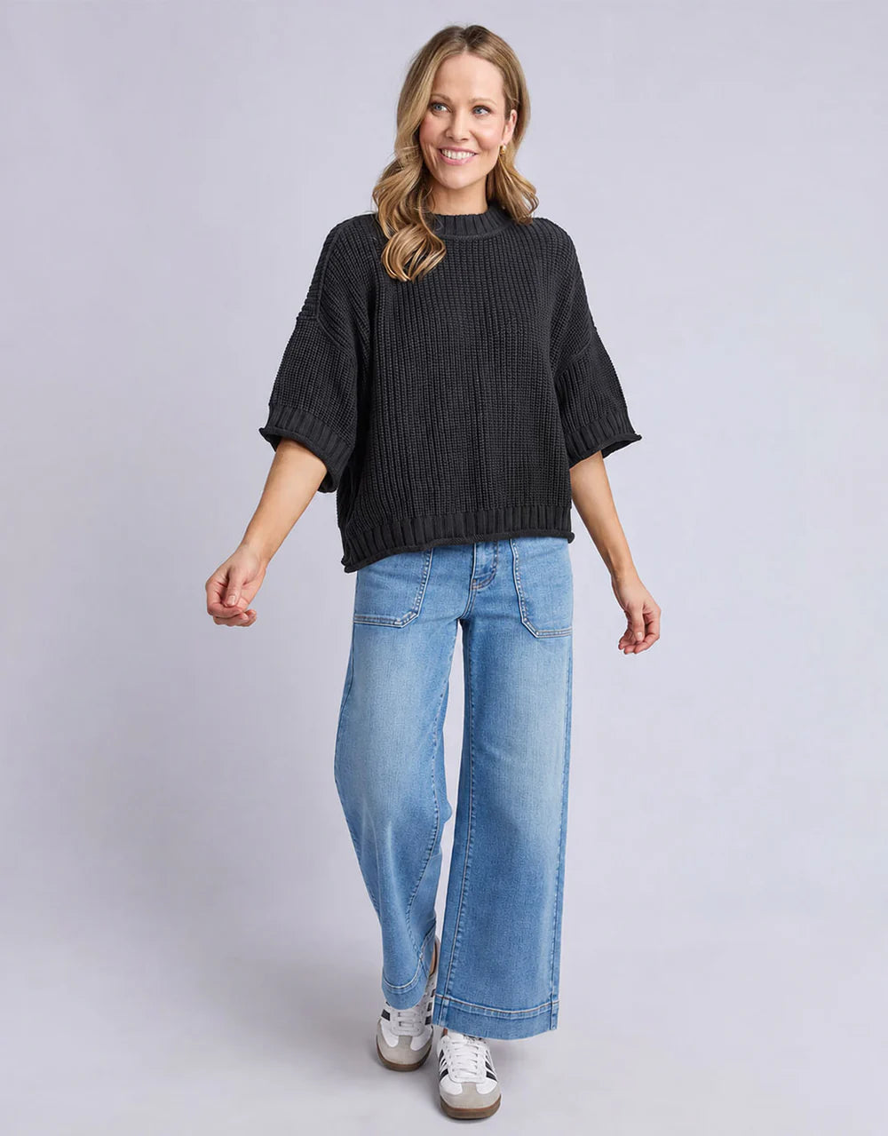 Woman wearing a Elm black sweater and blue jeans on a gray background