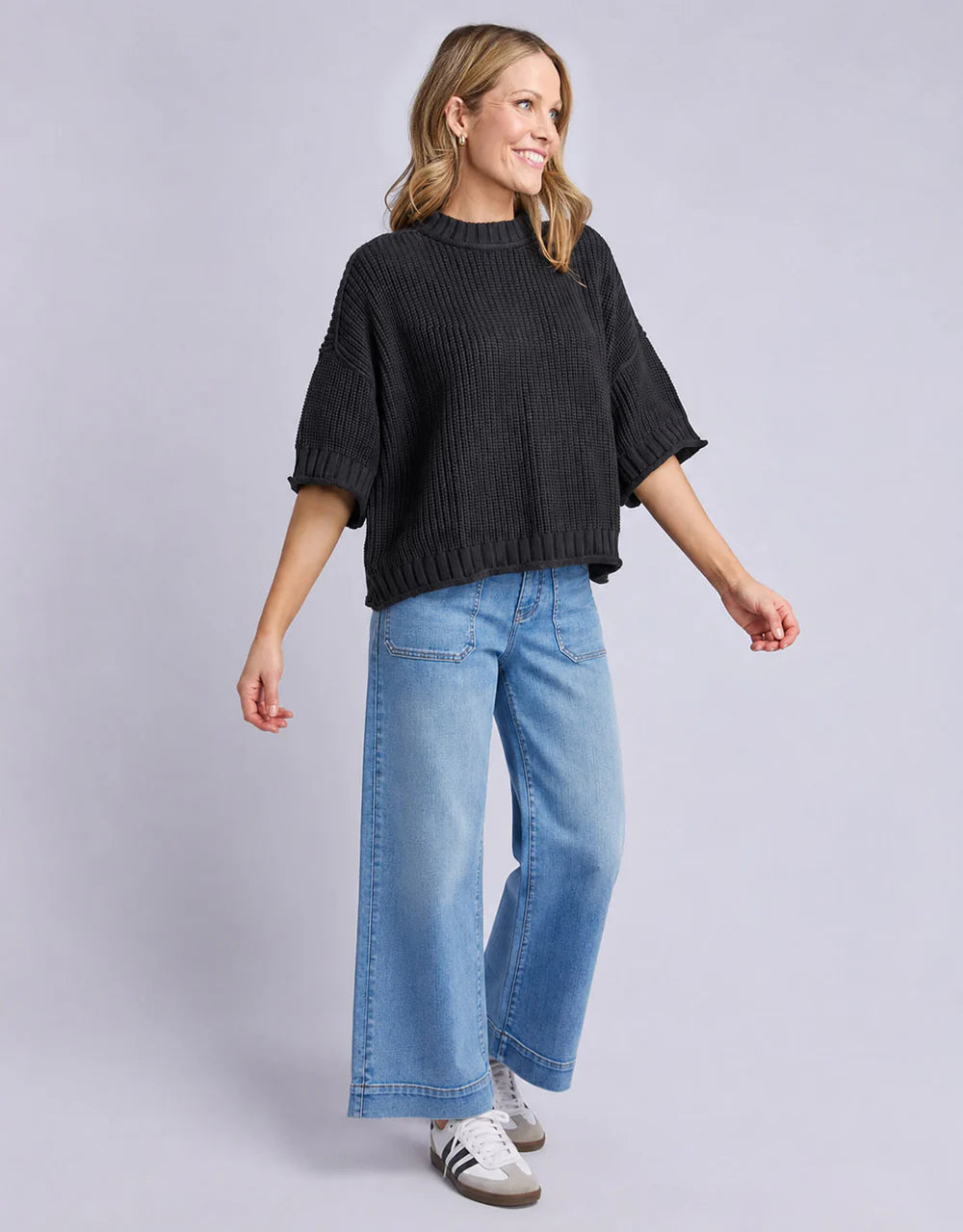 Woman wearing a Elm black sweater and blue jeans on a gray background