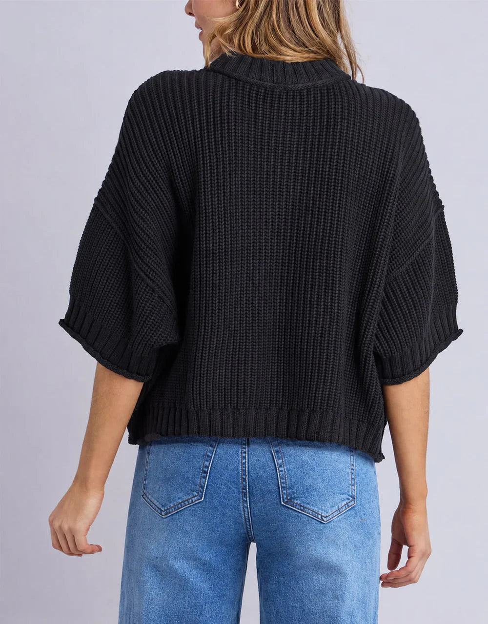 Woman wearing a Elm black knitted sweater and blue jeans on a light gray background