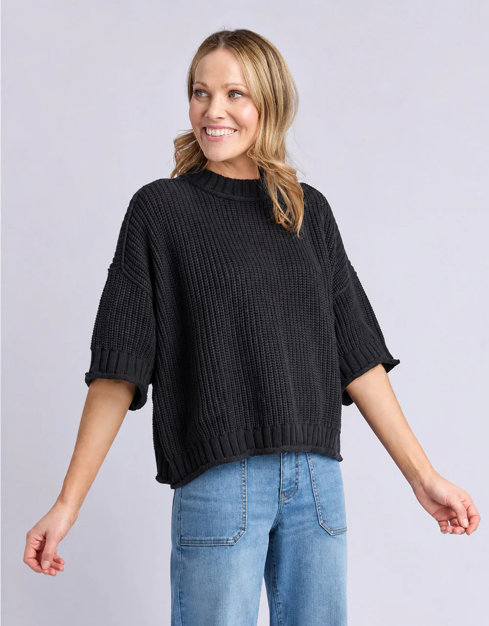 Image of Woman wearing a Elm black sweater and blue jeans on a light gray background