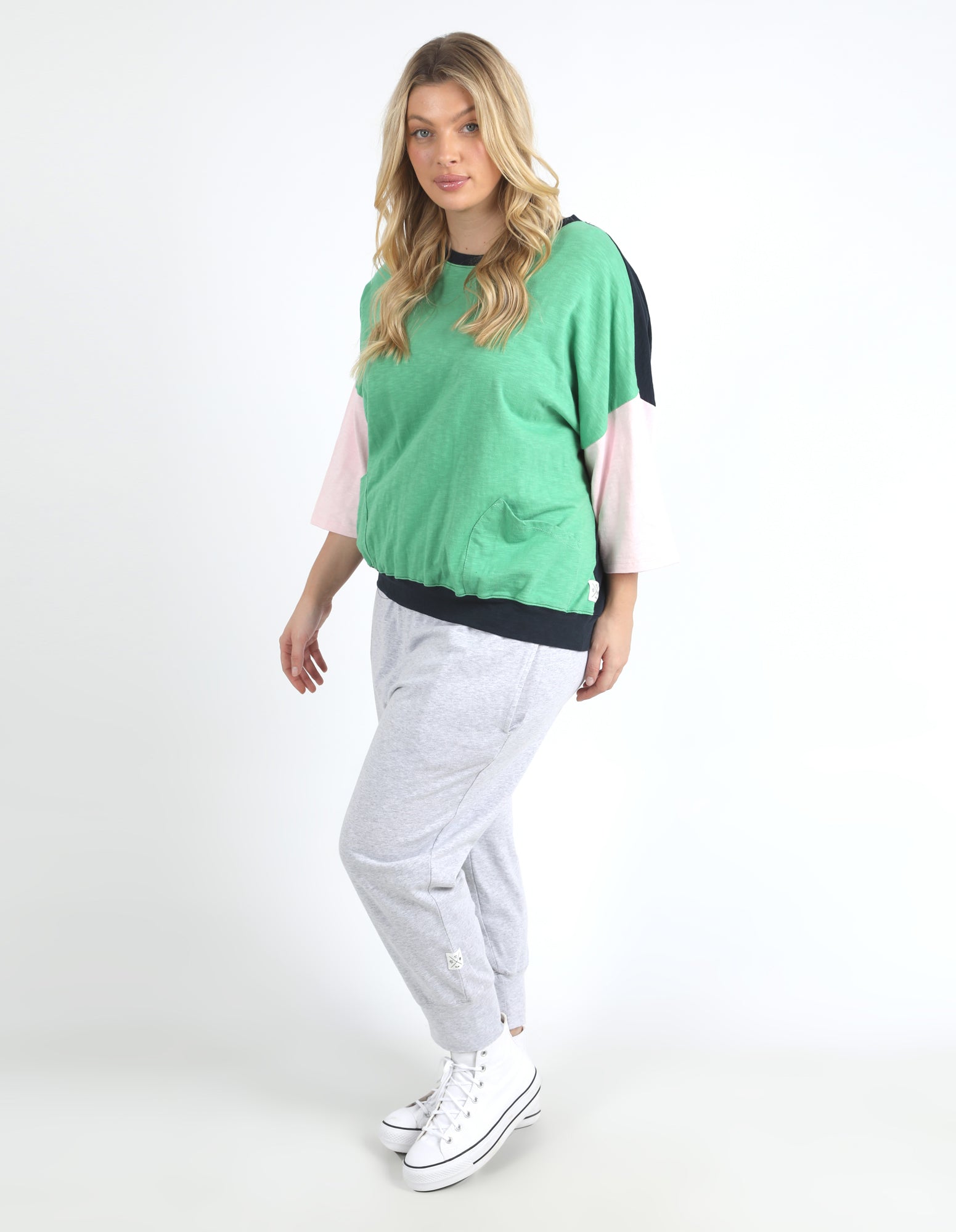 Image of Woman wearing a Elm green and black top with white pants on a white background