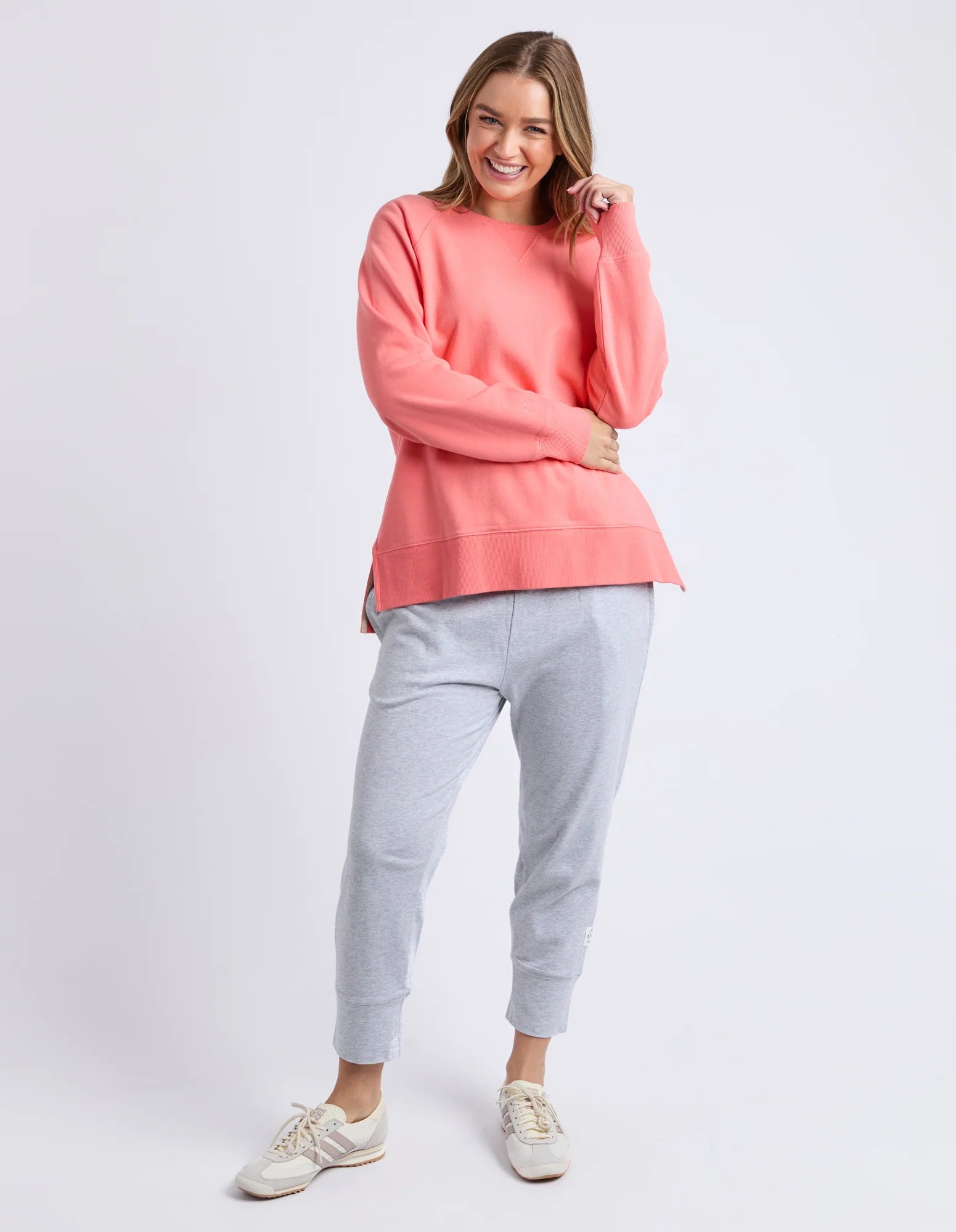 Image of Woman wearing a Elm coral sweatshirt and gray jogger pants on a white background