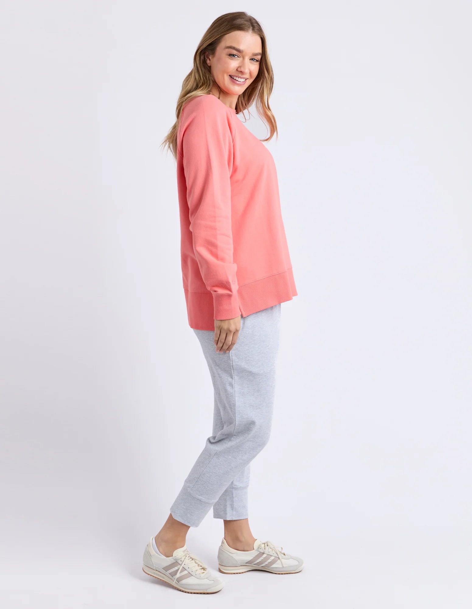 Image of Woman wearing a Elm coral top and light gray pants on a white background