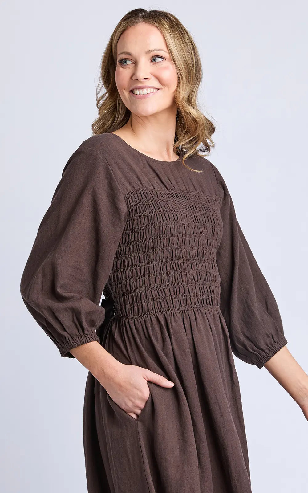 Woman wearing a Elm brown dress with puffed sleeves on a light gray background