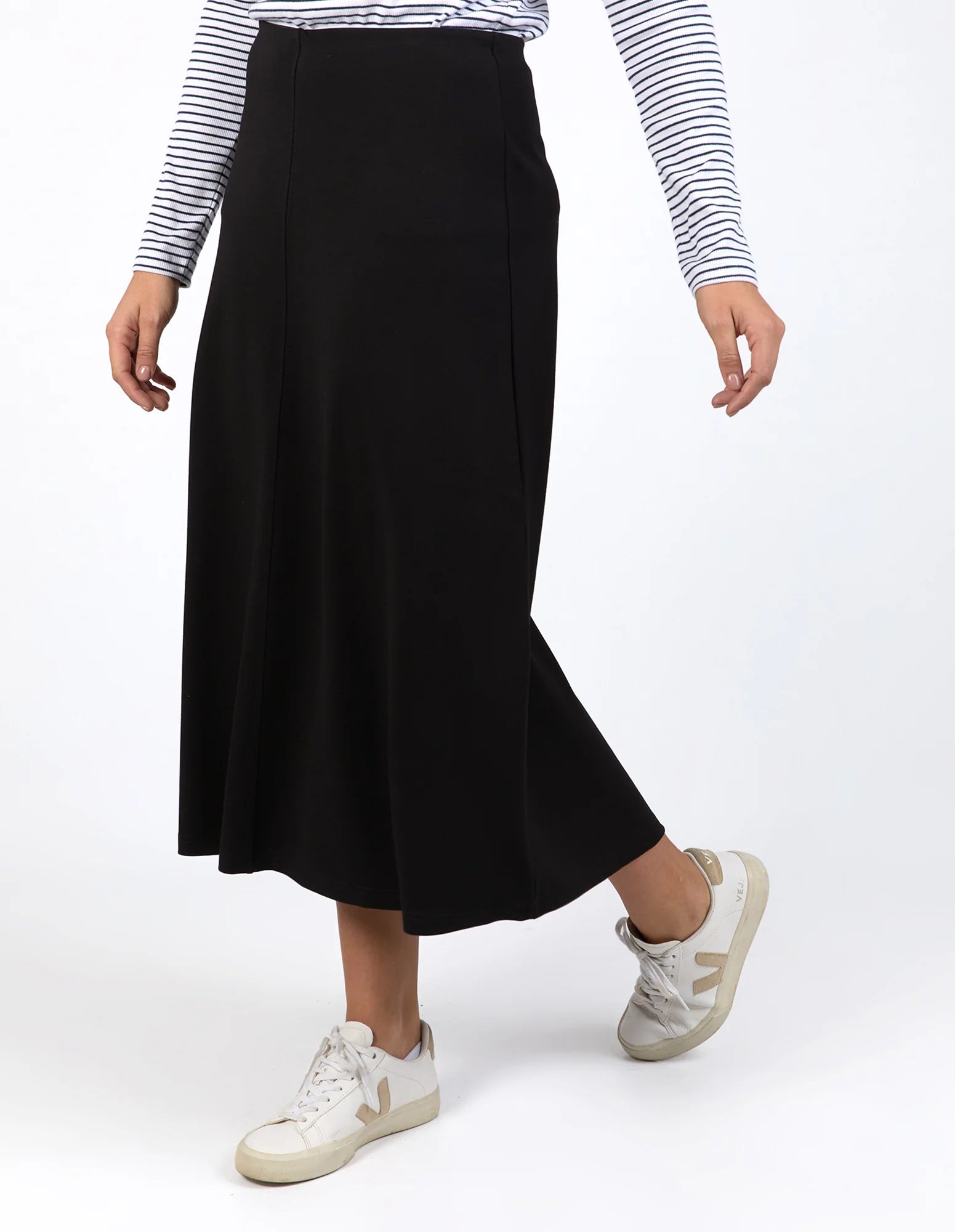 Woman wearing a Elm black skirt with a striped shirt and white sneakers on a white background