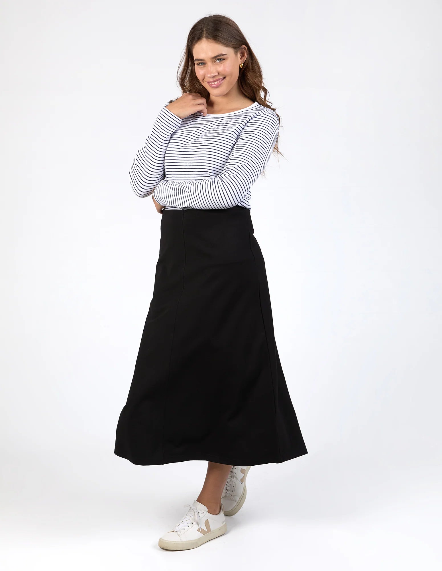 Woman wearing a Elm black skirt and striped shirt on a white background