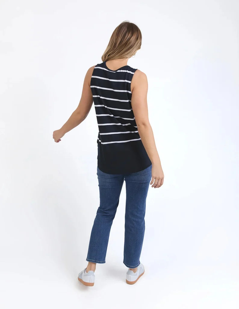 Image of A woman shown from the back wearing a Elm sleeveless black top with thin white horizontal stripes, blue jeans, and white sneakers, photographed against a plain white studio background.