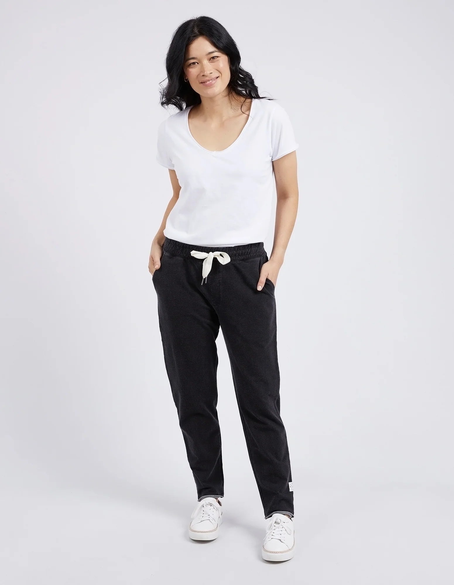 Woman wearing a white t-shirt and Elm black pants on a plain background