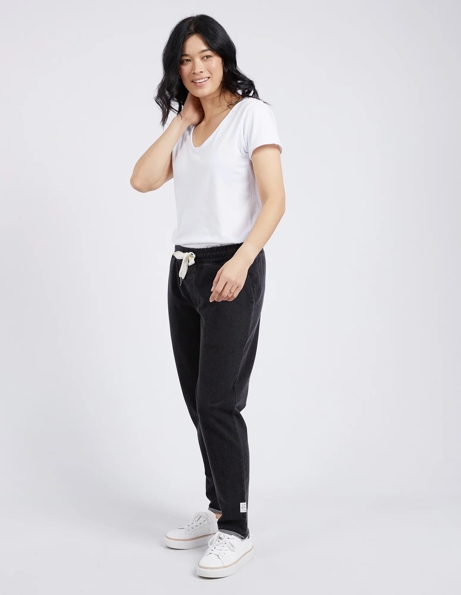 Woman wearing a white t-shirt and Elm black pants on a plain background