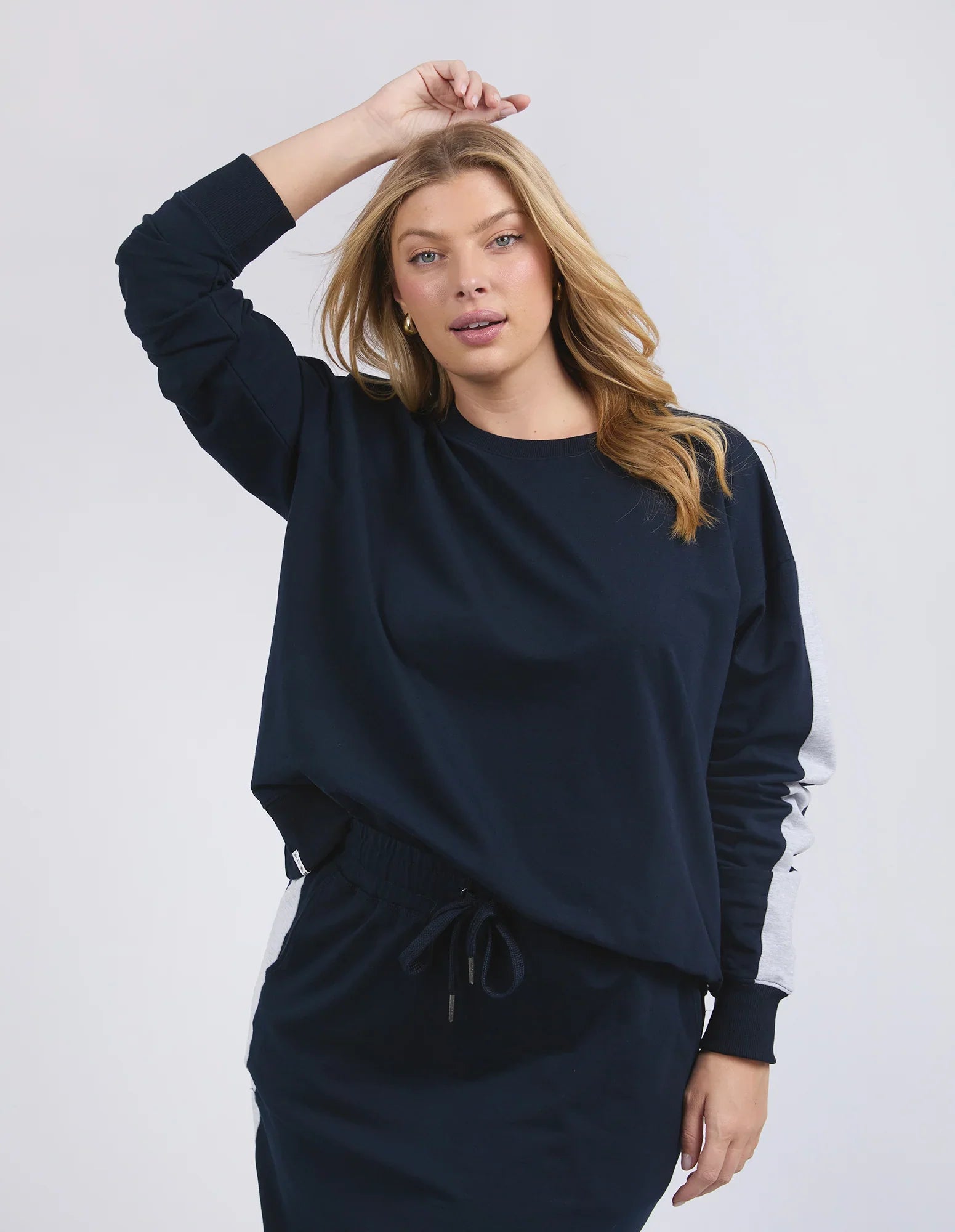 A woman modeling a Elm dark navy blue sweatshirt and matching sweatpants set against a light gray studio background.