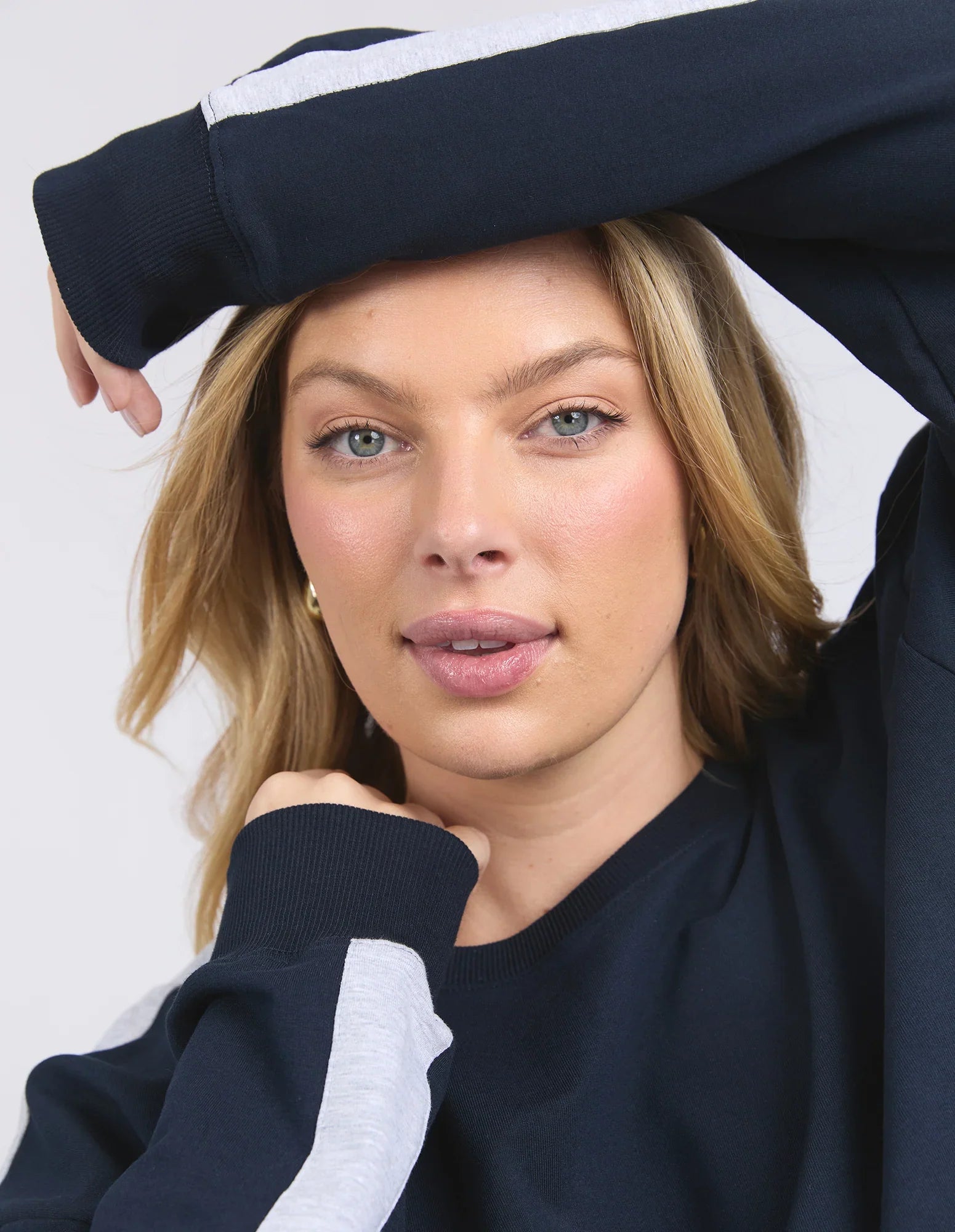 Image of A close-up of a woman wearing a Elm navy blue sweatshirt with a white stripe detail on the sleeve, posed against a light gray background.