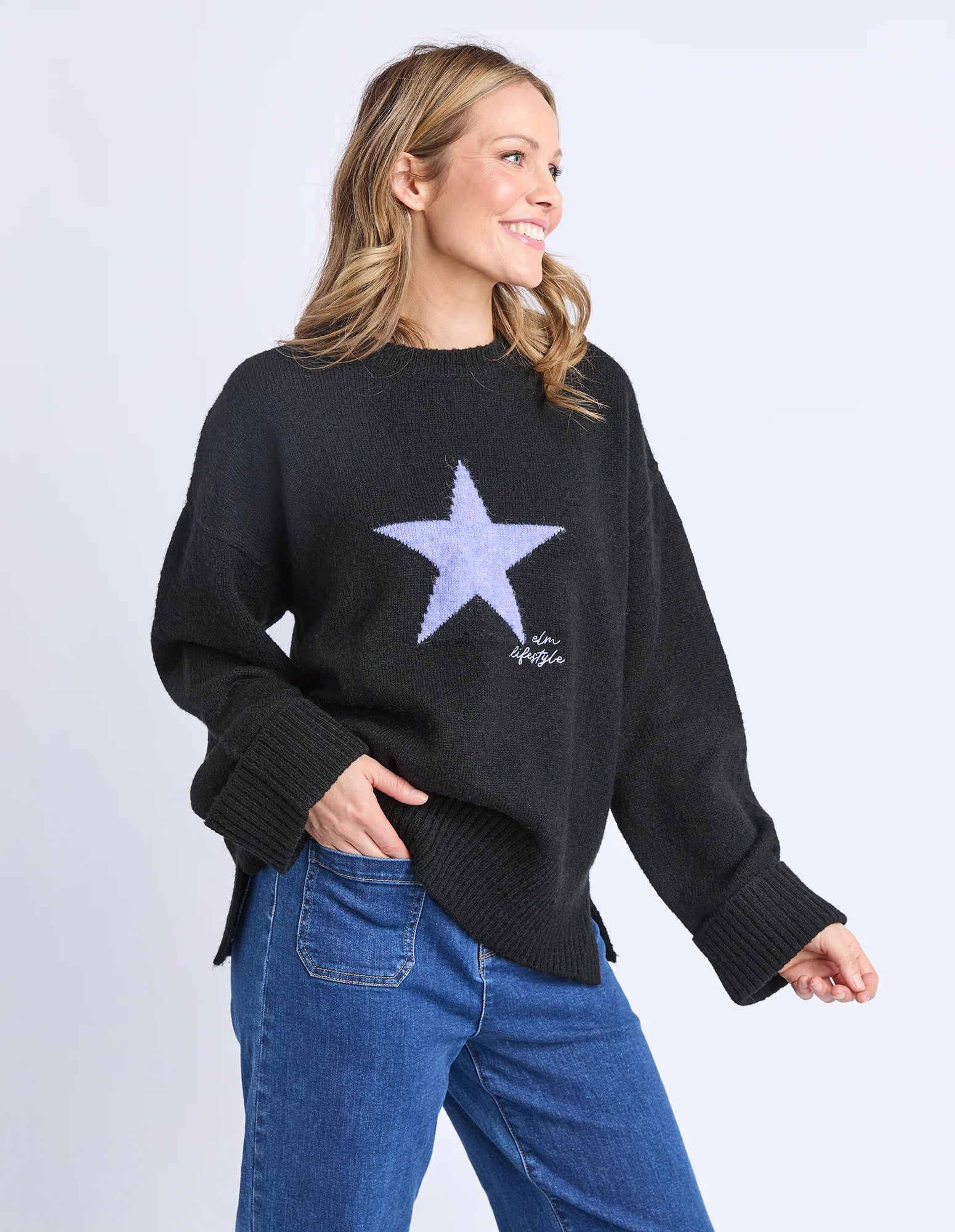 Woman wearing a Elm black sweater with a star design on a plain background