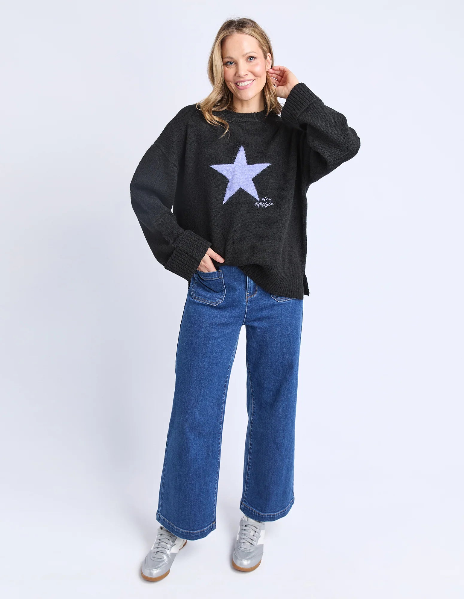 Woman wearing a Elm black sweater with a star design and blue jeans on a white background