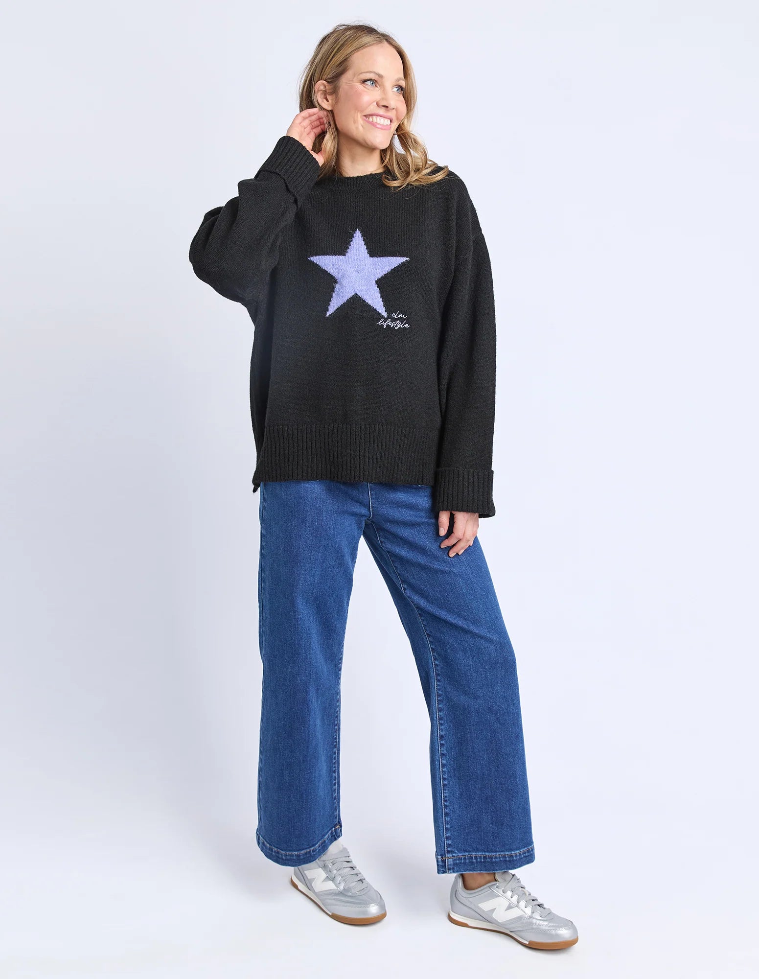 Image of Woman wearing a Elm black sweater with a star design and blue jeans on a white background