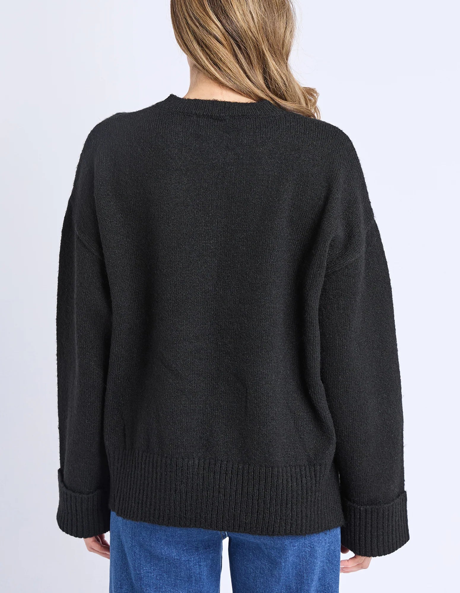 Woman wearing a Elm black sweater with a plain background