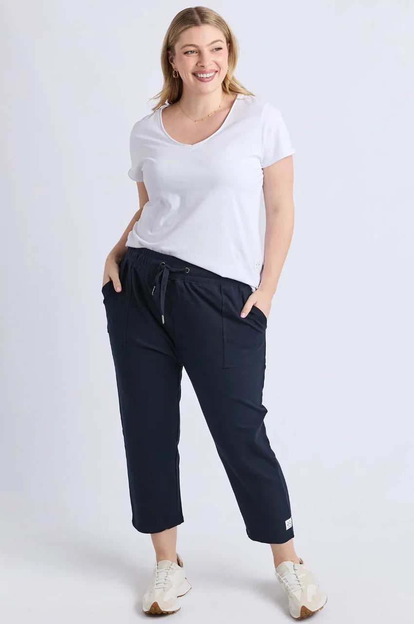 Image of A woman modeling a white short-sleeve V-neck t-shirt and Elm dark navy cropped drawstring pants with side pockets, paired with white sneakers, against a light gray studio background.