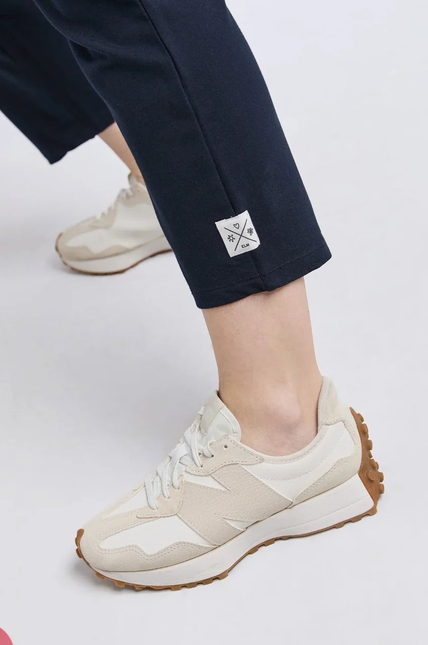 Image of White sneakers with brown soles worn with Elm navy pants on a white background