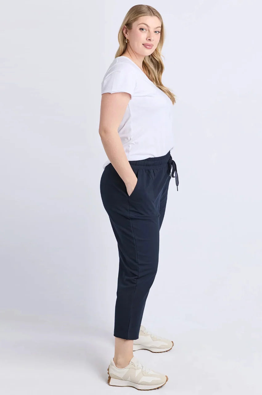 Image of A woman modeling Elm dark navy cropped pants with a drawstring waist, paired with a white t-shirt and white sneakers, standing against a light gray studio background.
