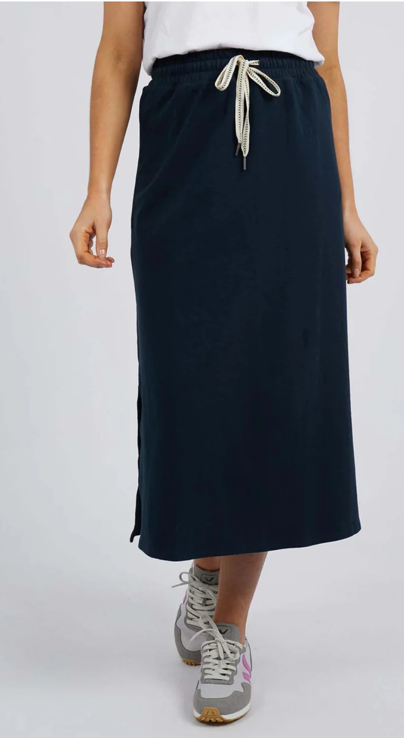Image of A woman wearing a Elm dark navy midi skirt with a cream drawstring, paired with a white top and gray sneakers, shown from the waist down against a light gray studio background.