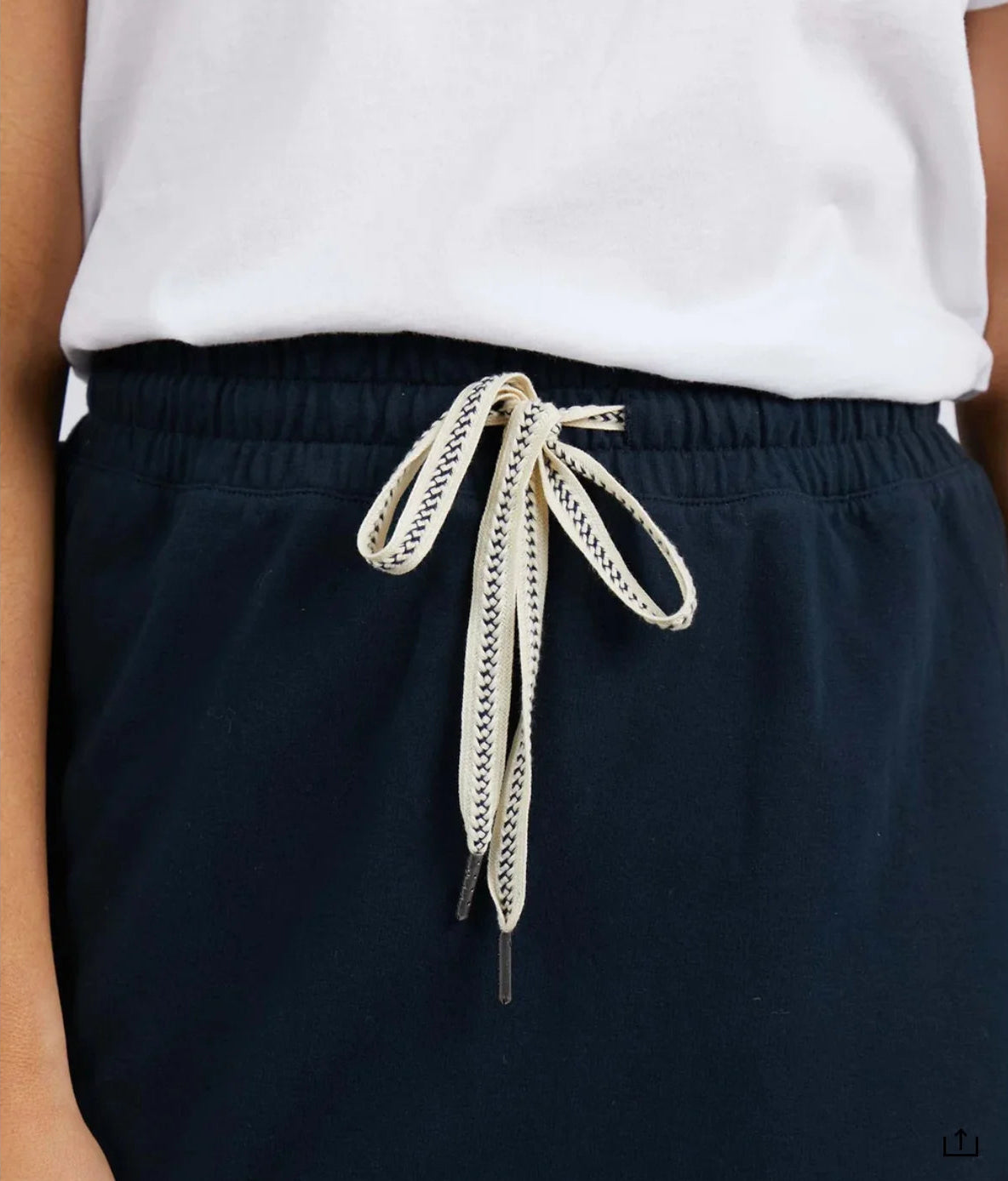 Image of Close-up of a woman wearing Elm dark navy drawstring shorts with a white top, showing the elastic waistband and cream drawstring with a black zigzag pattern.