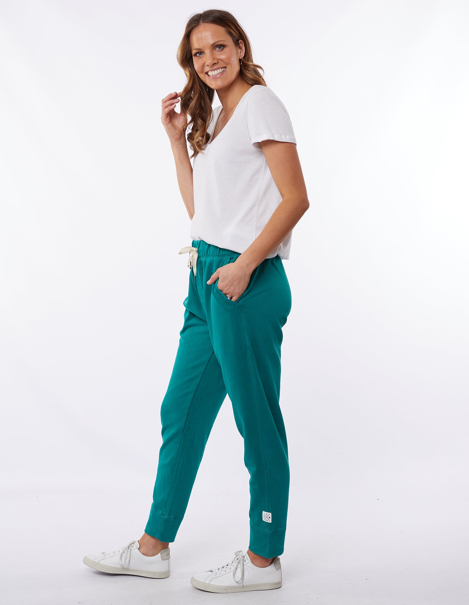 Image of Woman wearing a pair of winter green Elm Victoria pants with an elastic waistband and tapered leg, worn with white sneakers.