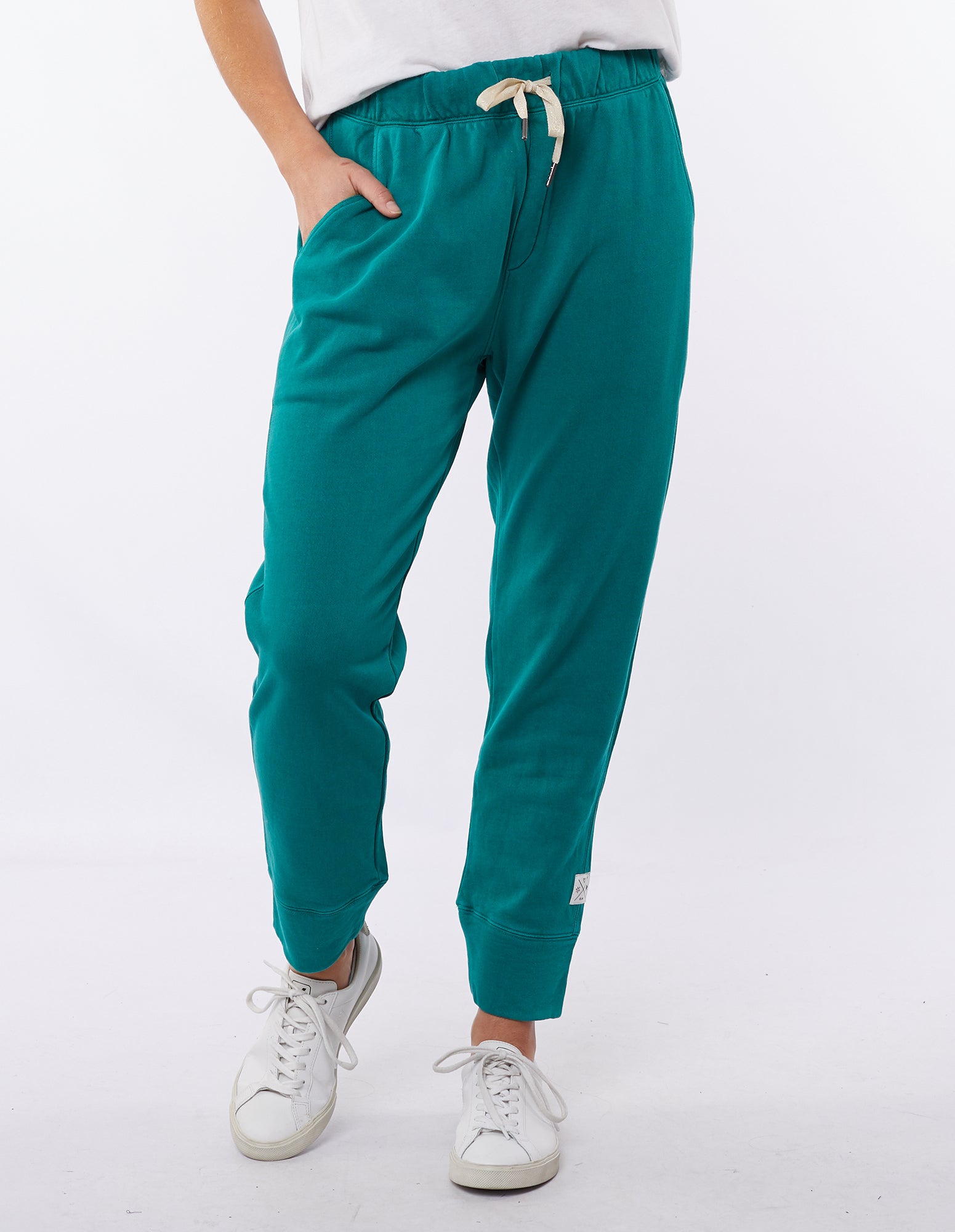 Image of A pair of winter green Elm Victoria pants with an elastic waistband and tapered leg, worn with white sneakers.