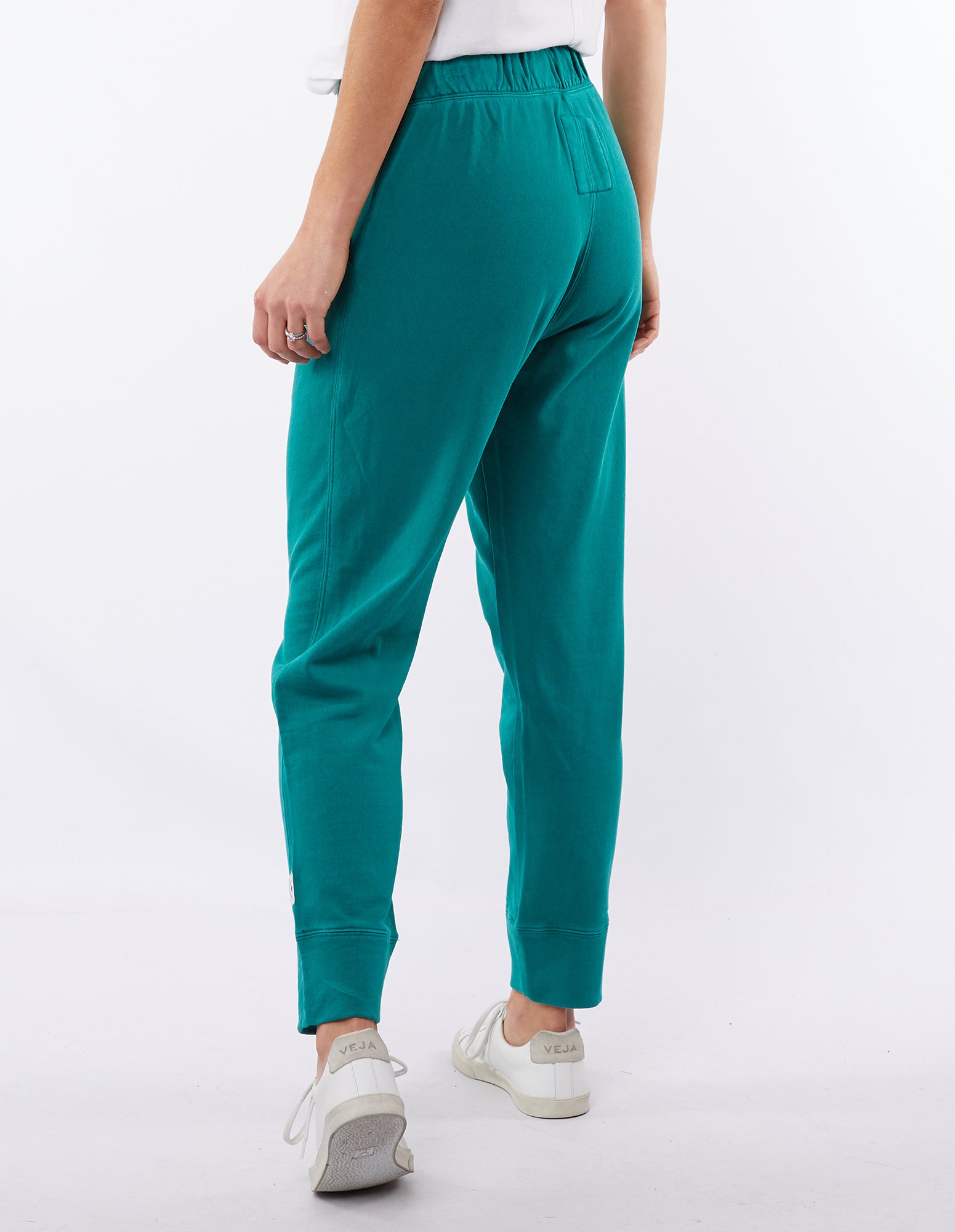 Image of Woman wearing a pair of winter green Elm Victoria pants with an elastic waistband and tapered leg, worn with white sneakers.