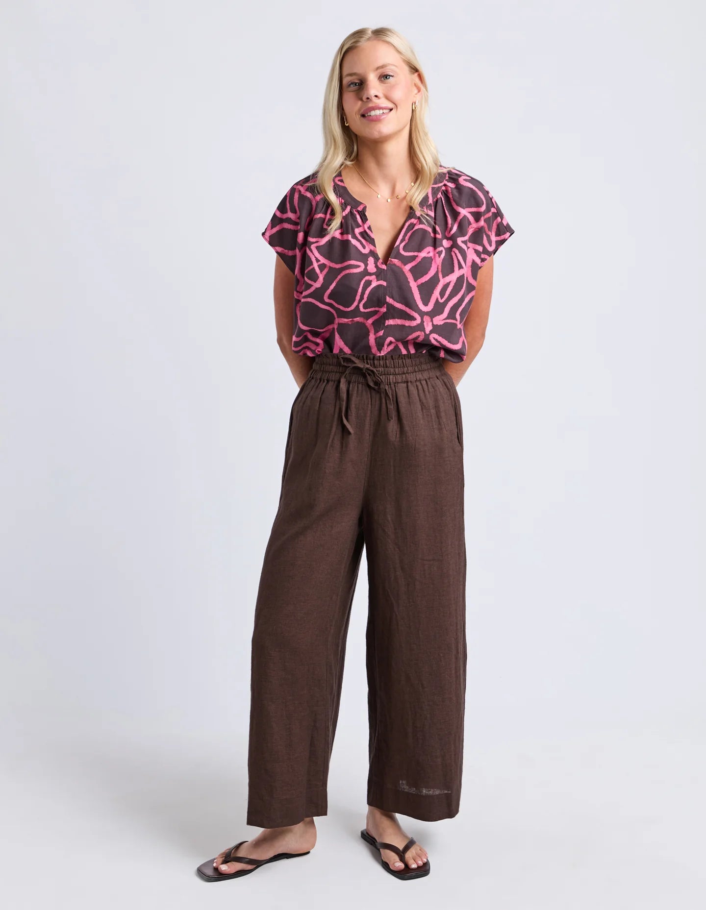 Image of Woman wearing Elm chocolate brown wide leg pants paired with a printed blouse on a plain background 