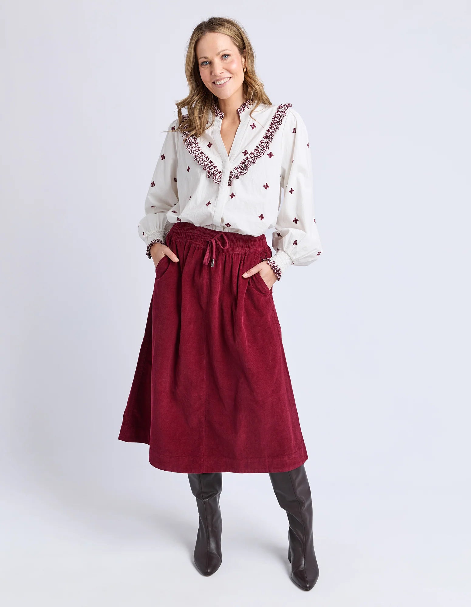 Image of Woman wearing a white blouse with red embroidery and a Elm red skirt on a white background