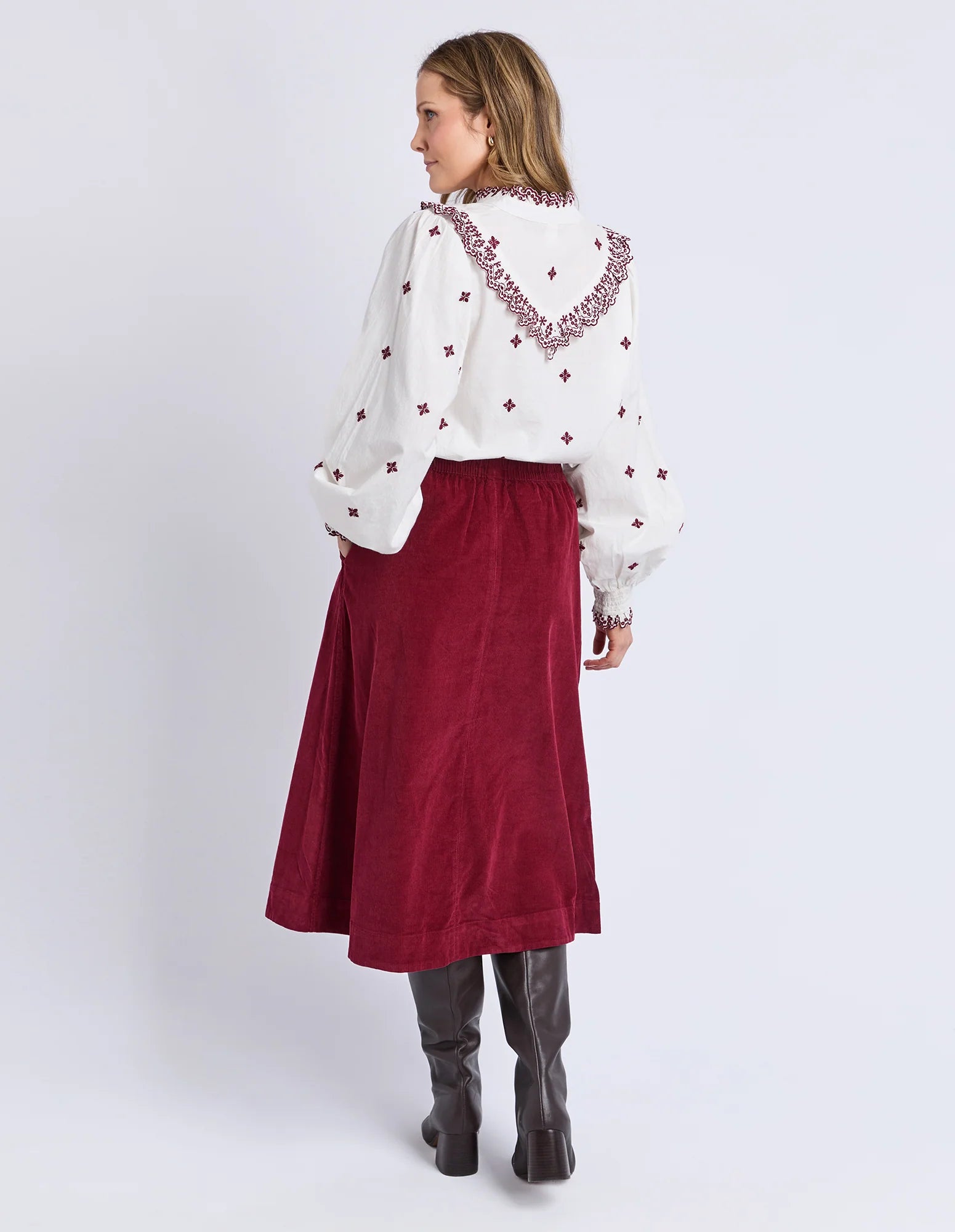 Woman wearing a white blouse with red embroidery and a Elm red skirt on a white background