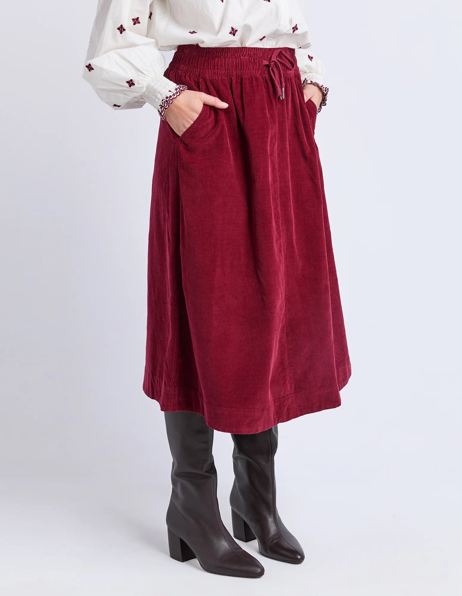 Image of Elm red skirt worn with a white blouse and black boots on a light gray background