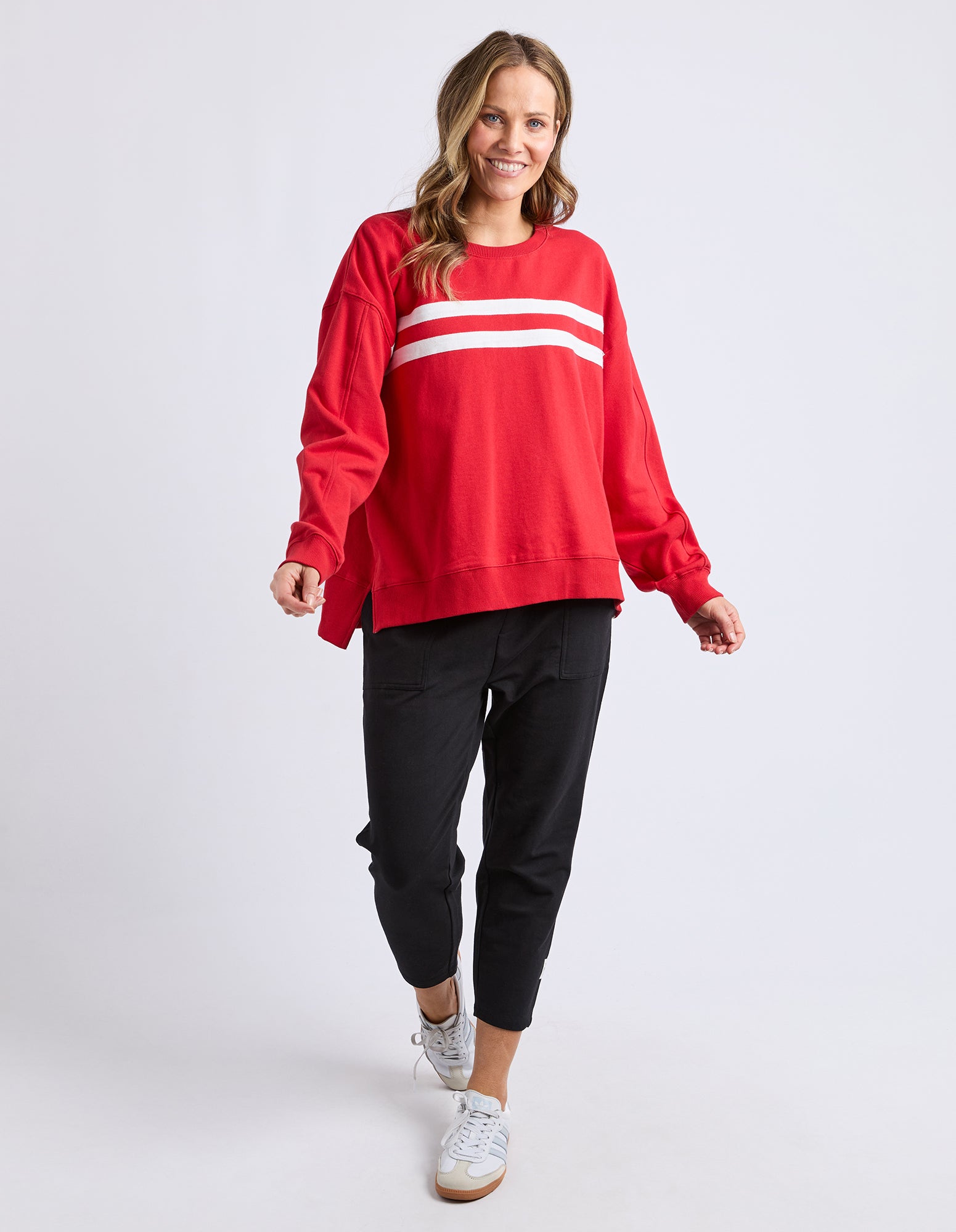 Image of Woman wearing a red crew neck jumper with white stripes and black pants on a white background