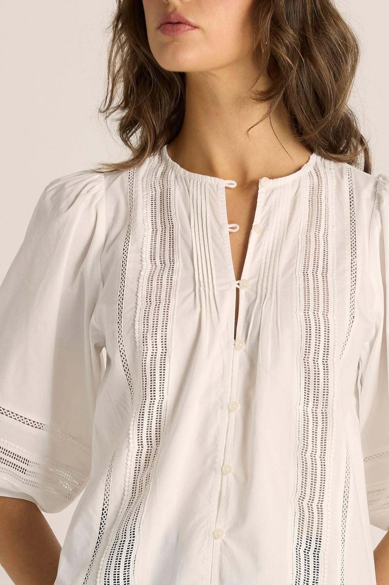 Image of A close-up of a woman wearing a Fate & Becker white short-sleeve blouse with vertical eyelet lace panels and a split neckline.