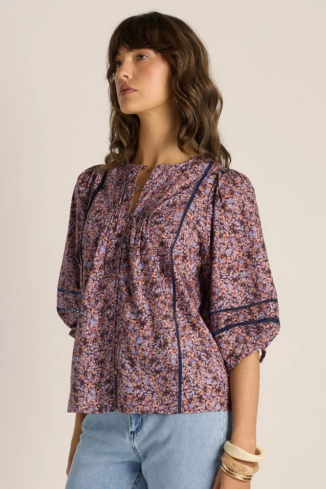 Woman wearing a Fate & Becker patterned blouse with rolled-up sleeves against a beige background